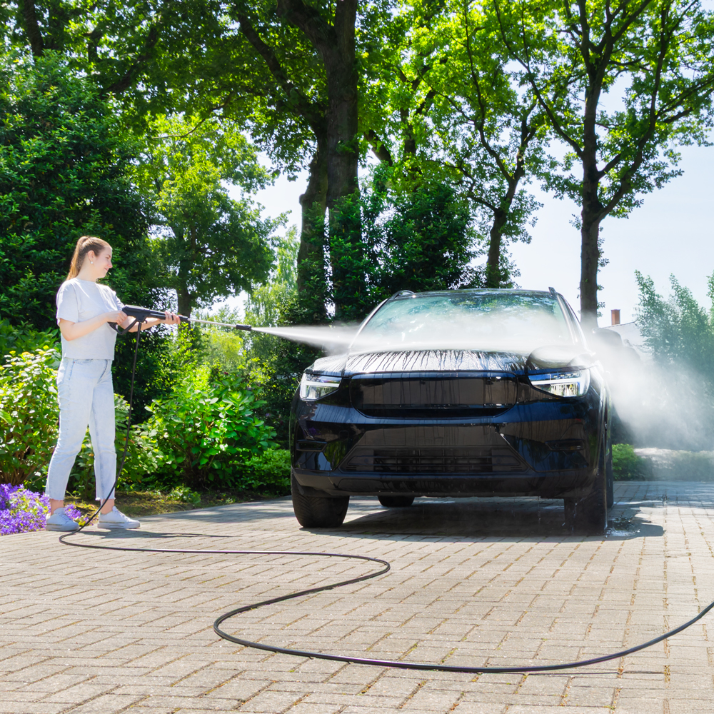 Een vrouw wast buiten een zwarte auto met een hogedrukreiniger.