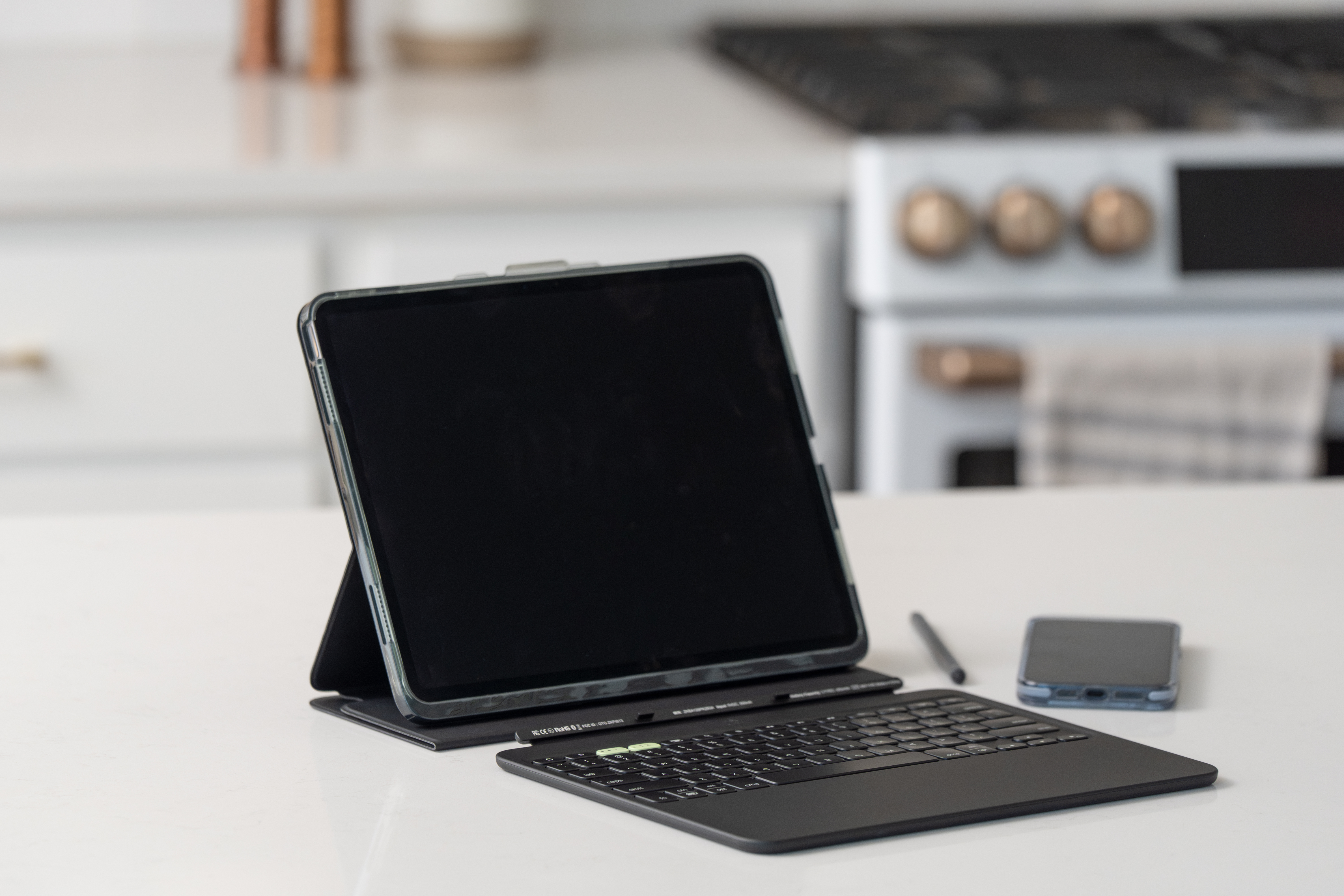 Ein Tablet mit Tastatur und Stift liegt auf einem Tisch. Eine Smartphone im Hintergrund.