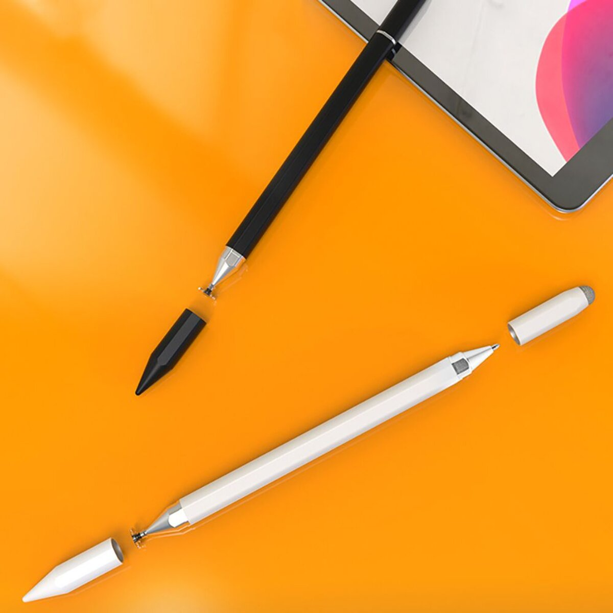 Zwei Stifte, schwarz und weiß, liegen auf einem orangefarbenen Untergrund neben einem Tablet.