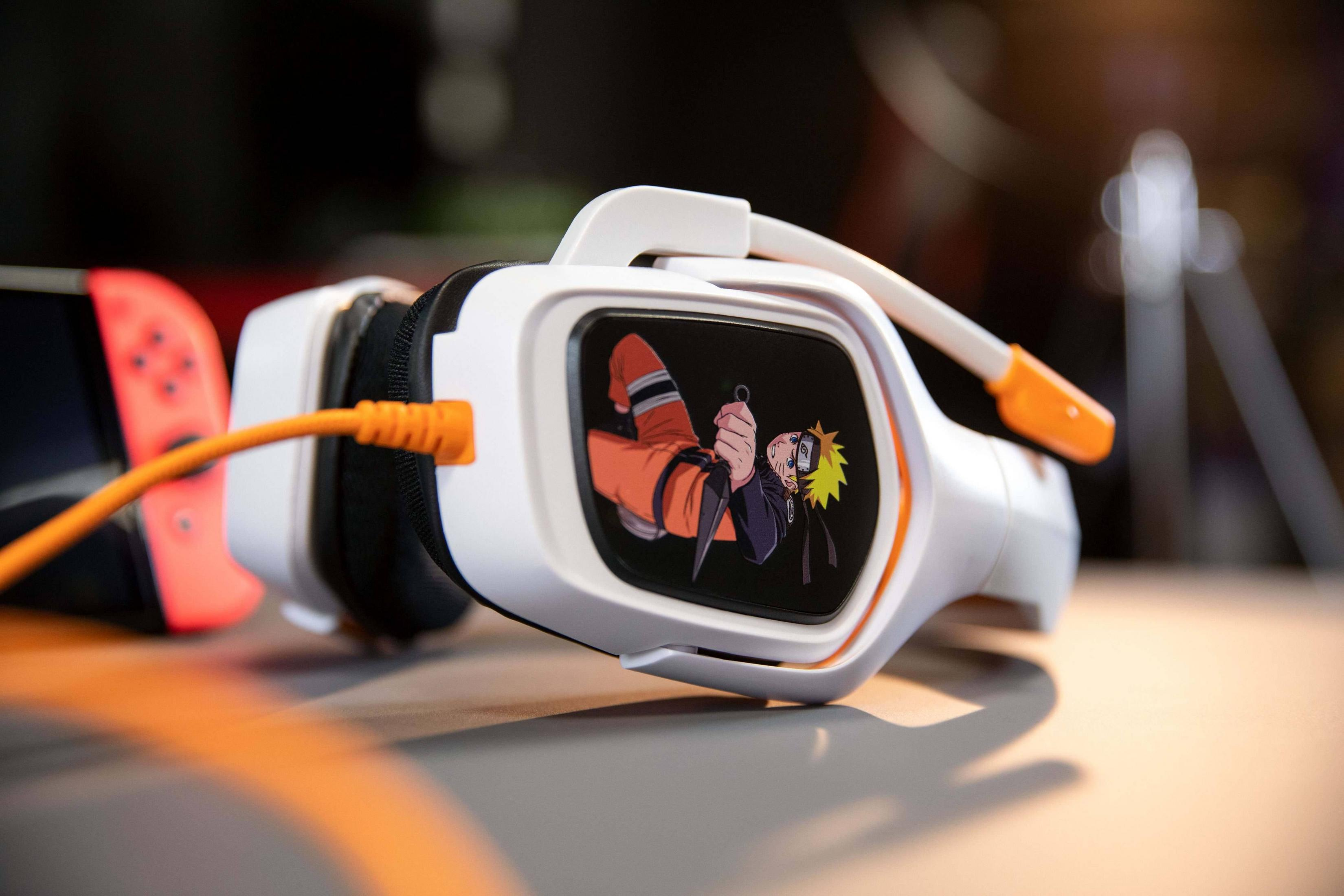 Weiße Kopfhörer mit Naruto-Aufkleber und orangefarbenem Kabel neben einem Nintendo Switch.