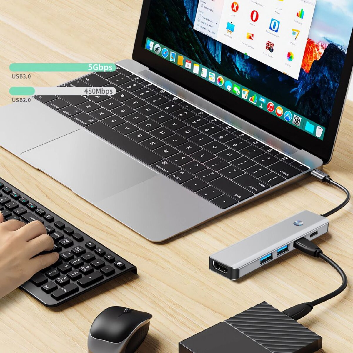 Un laptop con tastiera, mouse, hard disk e hub USB esterni su una scrivania di legno.