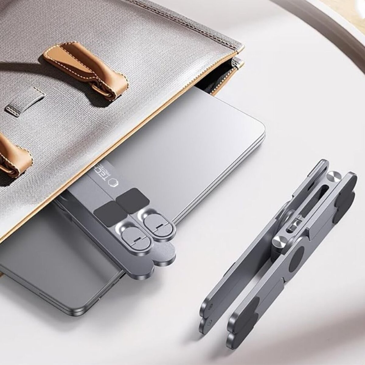 Ein silberner Laptopständer liegt neben einem Laptop in einer grauen Tasche.
