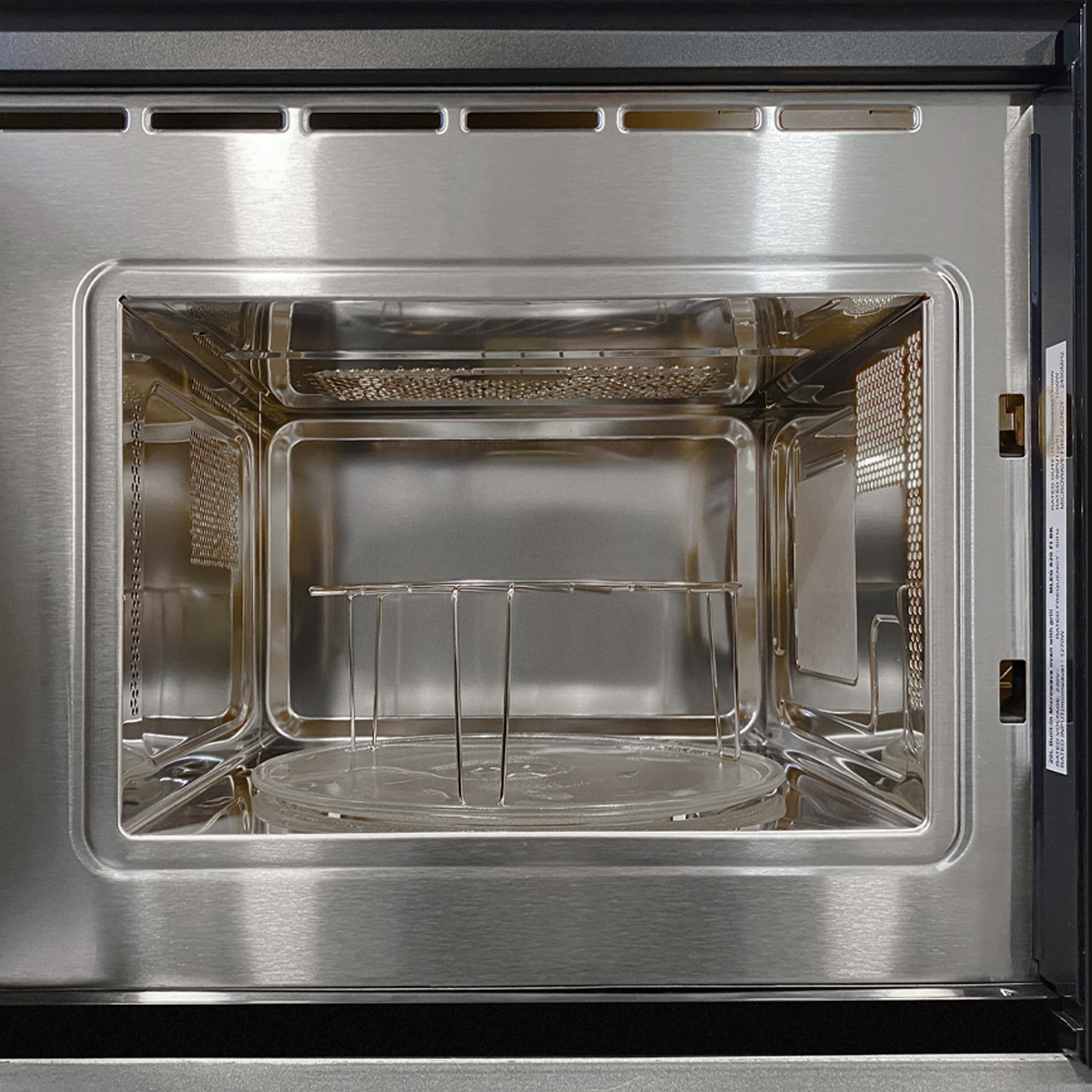 Vista interior de un microondas limpio y vacío de acero inoxidable con plato giratorio de cristal.