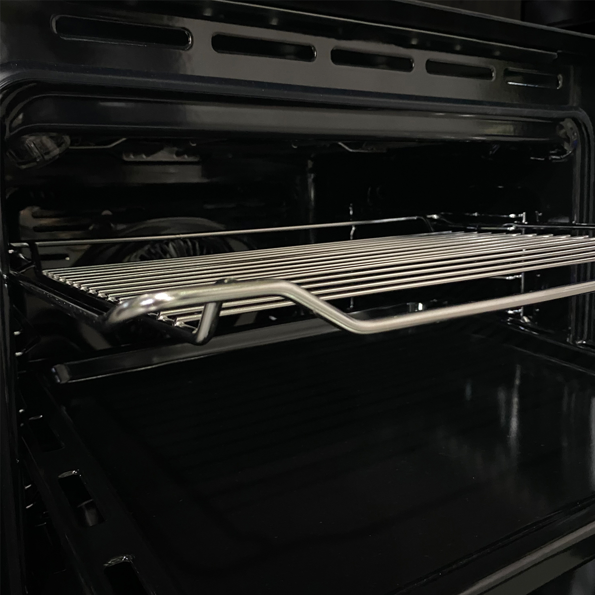 Vista interior de un horno negro con una rejilla metálica y una bandeja.