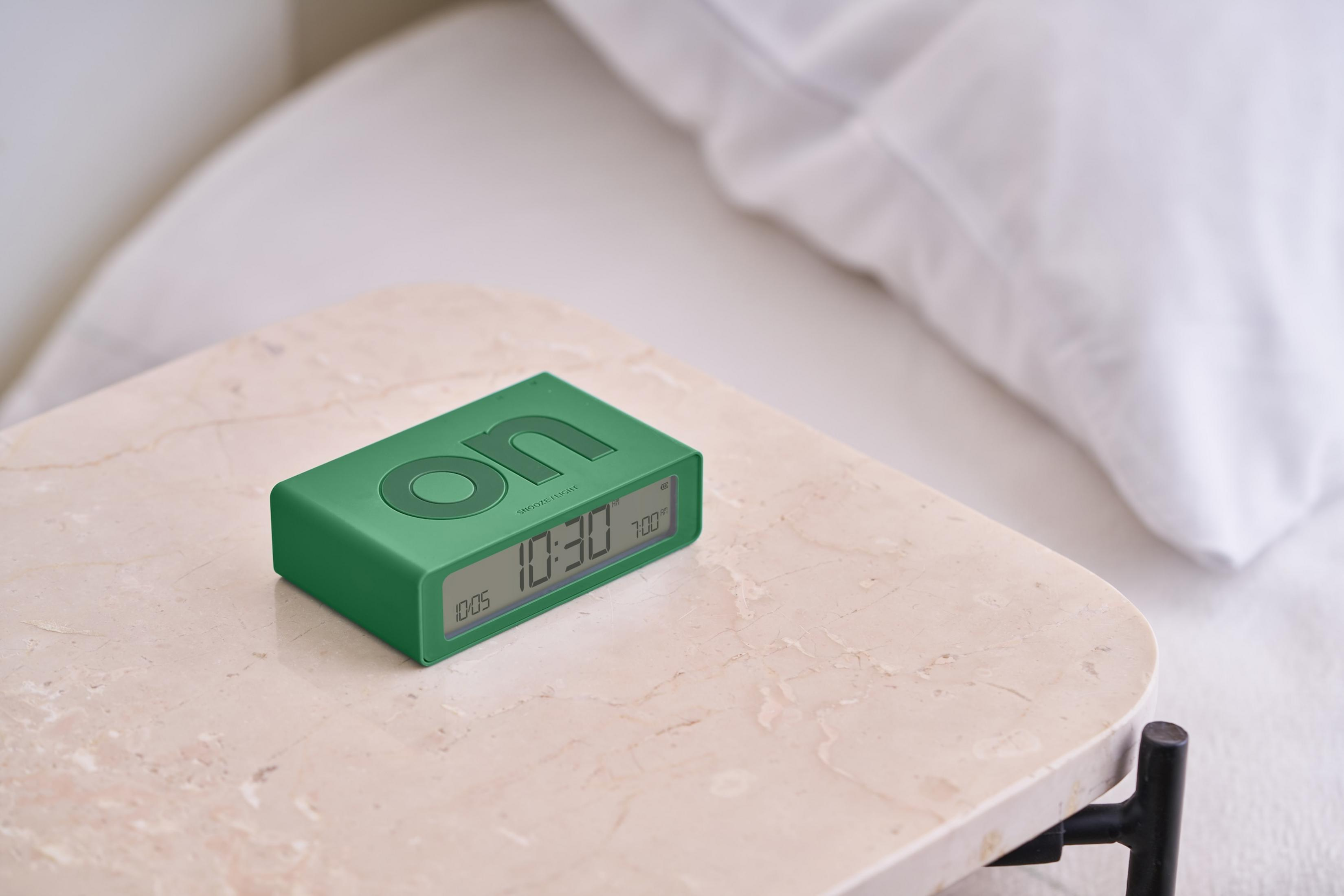 Réveil numérique vert sur table marbre près d'un oreiller blanc.