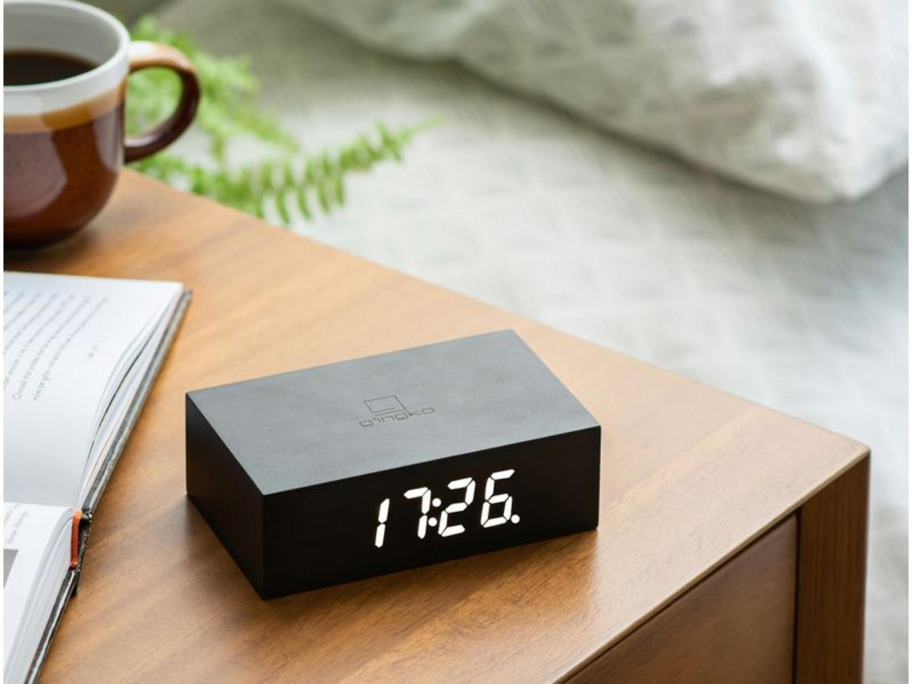 Schwarzer Digitalwecker zeigt 17:26 auf einem Holztisch neben einer Tasse.