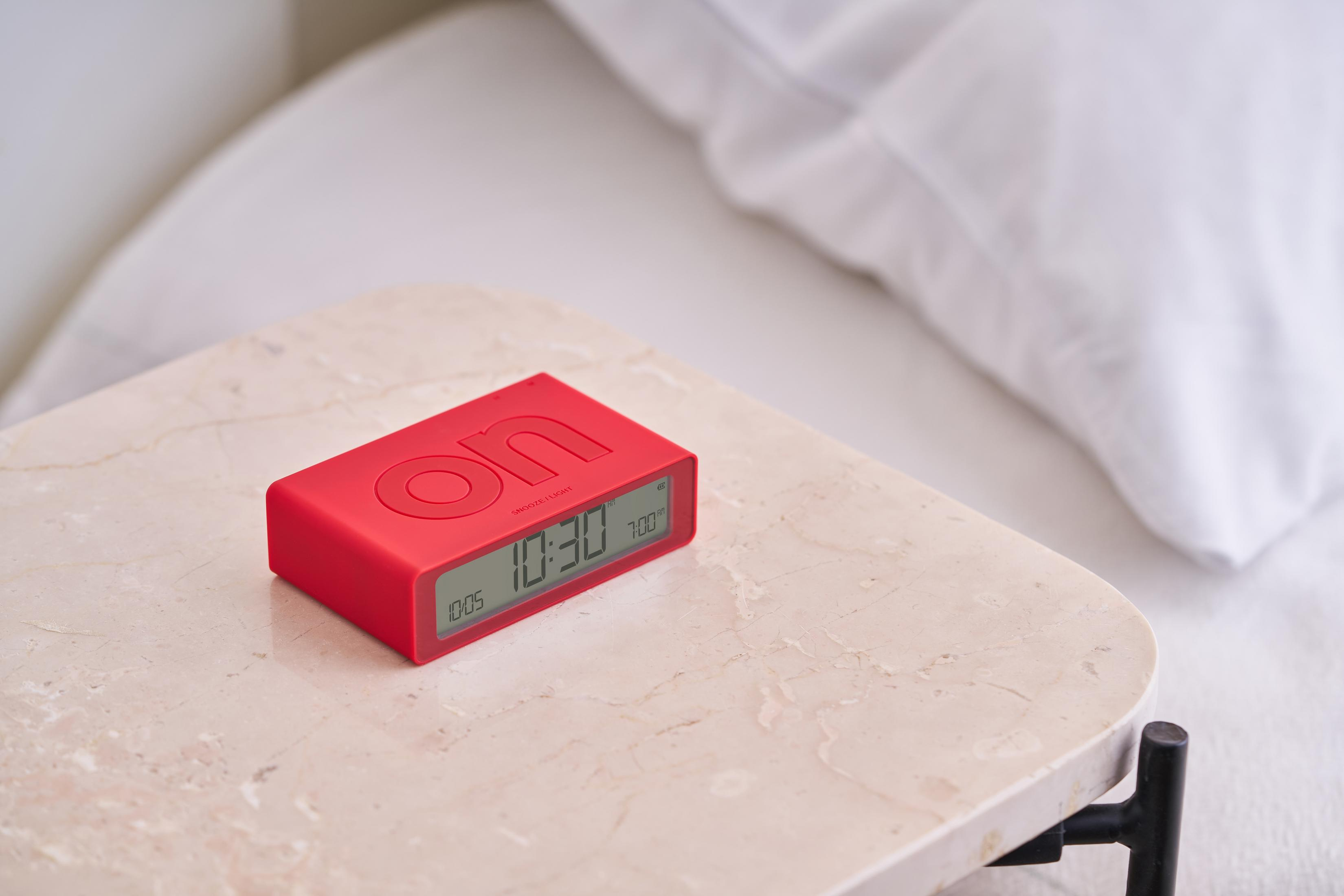 Ein roter Wecker auf einem Marmortisch neben einem weißen Bett.