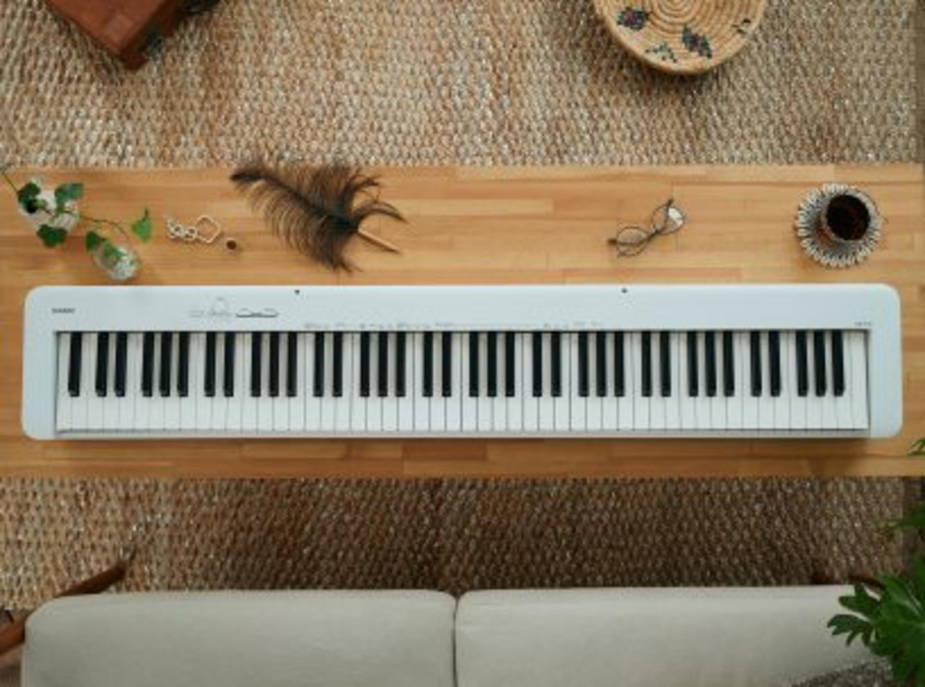 Ein weißes Keyboard liegt auf einem Holztisch, daneben Federn, Schmuck und Gläser.