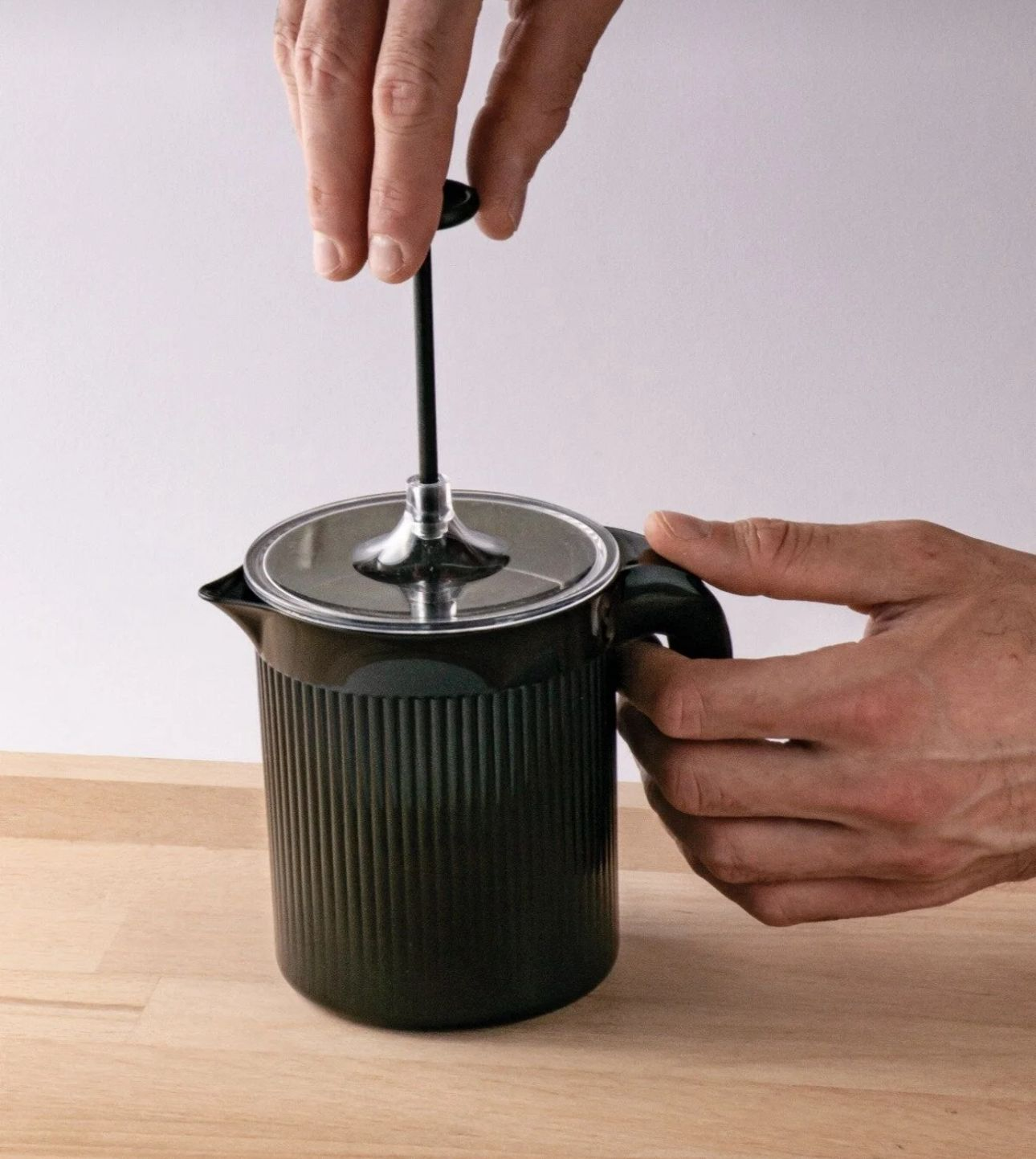Ahşap masa üzerinde siyah French press pistonunu bir el bastırıyor.