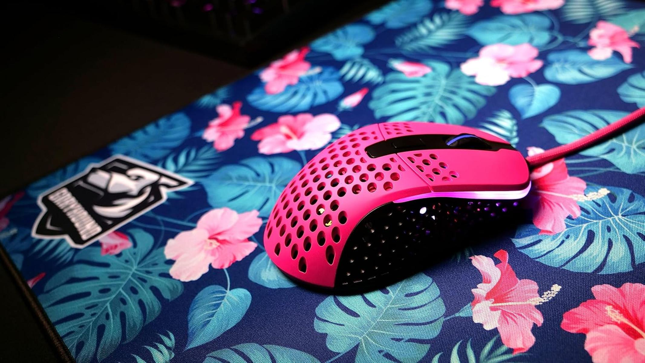 A pink gaming mouse rests on a mousepad with tropical leaves and hibiscus flowers.
