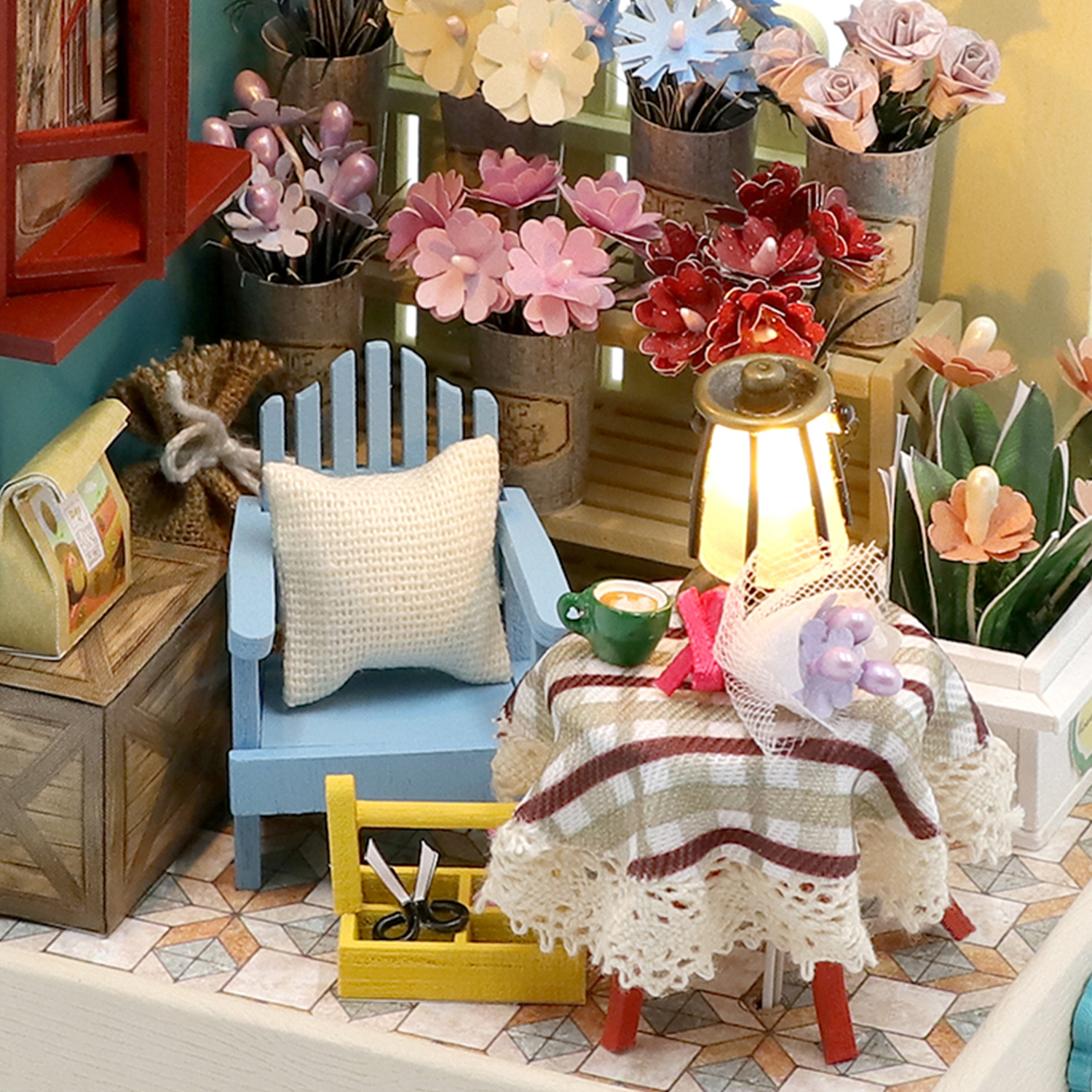 Scena in miniatura di un negozio di fiori con sedia, tavolo, lampade e fiori.