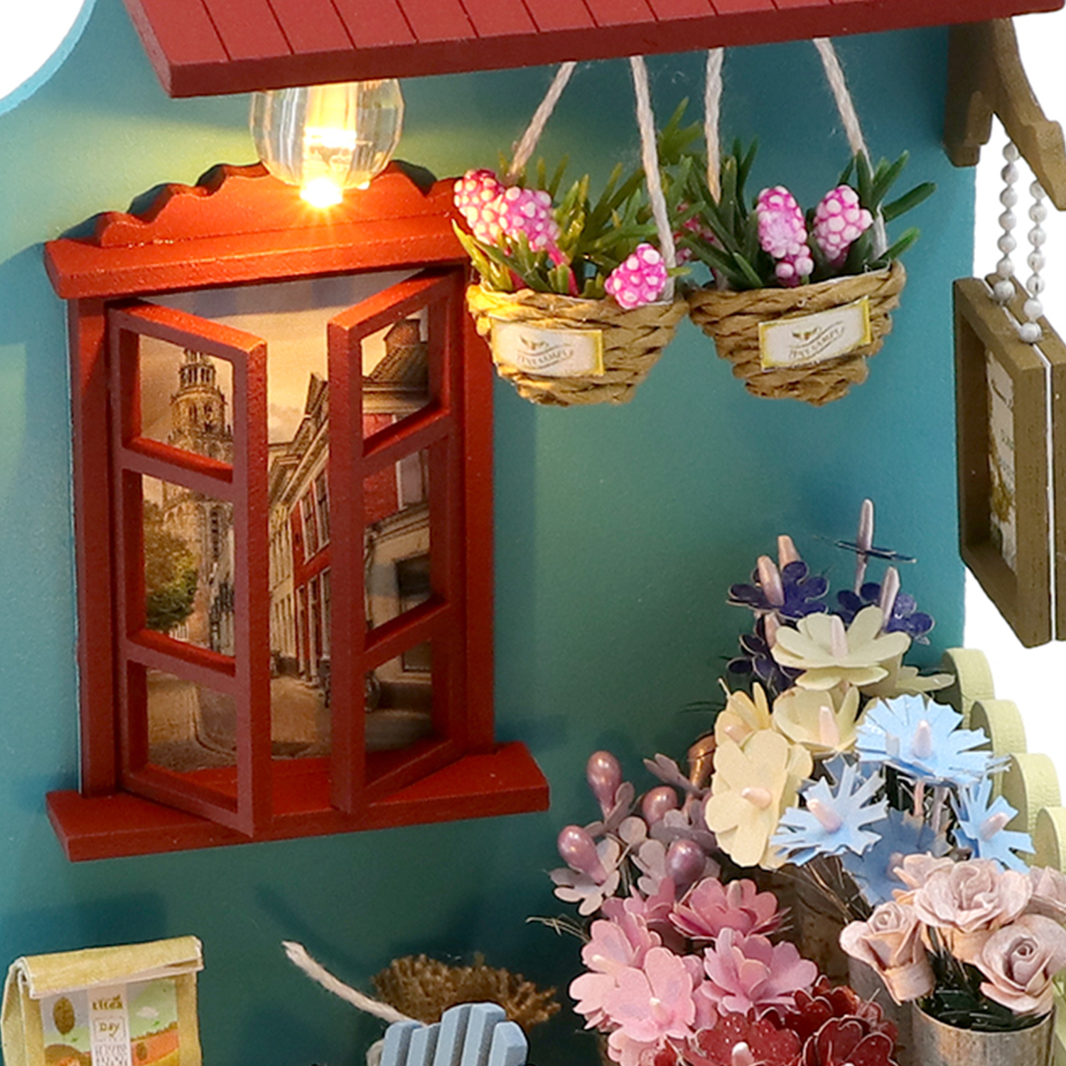 Casa in miniatura con finestra rossa, cesti di fiori appesi e fiori colorati.