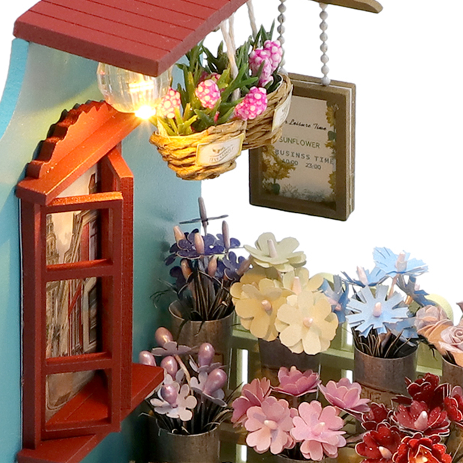 Casa in miniatura con tetto rosso, finestra, cesto di fiori rosa e fiori di carta in vaso.