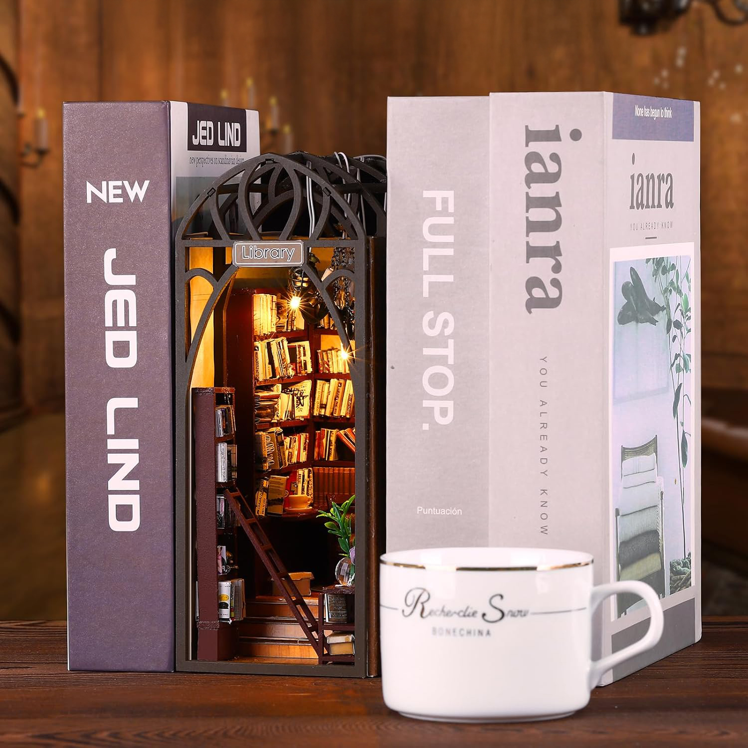 Libri, un modello di biblioteca in miniatura, una tazza e candele su un tavolo.