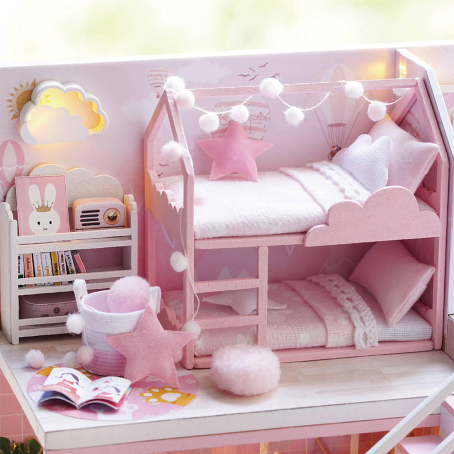 Una stanza rosa per casa delle bambole con letti a castello, una libreria e vari oggetti decorativi come una luce a nuvola e pom-pom.