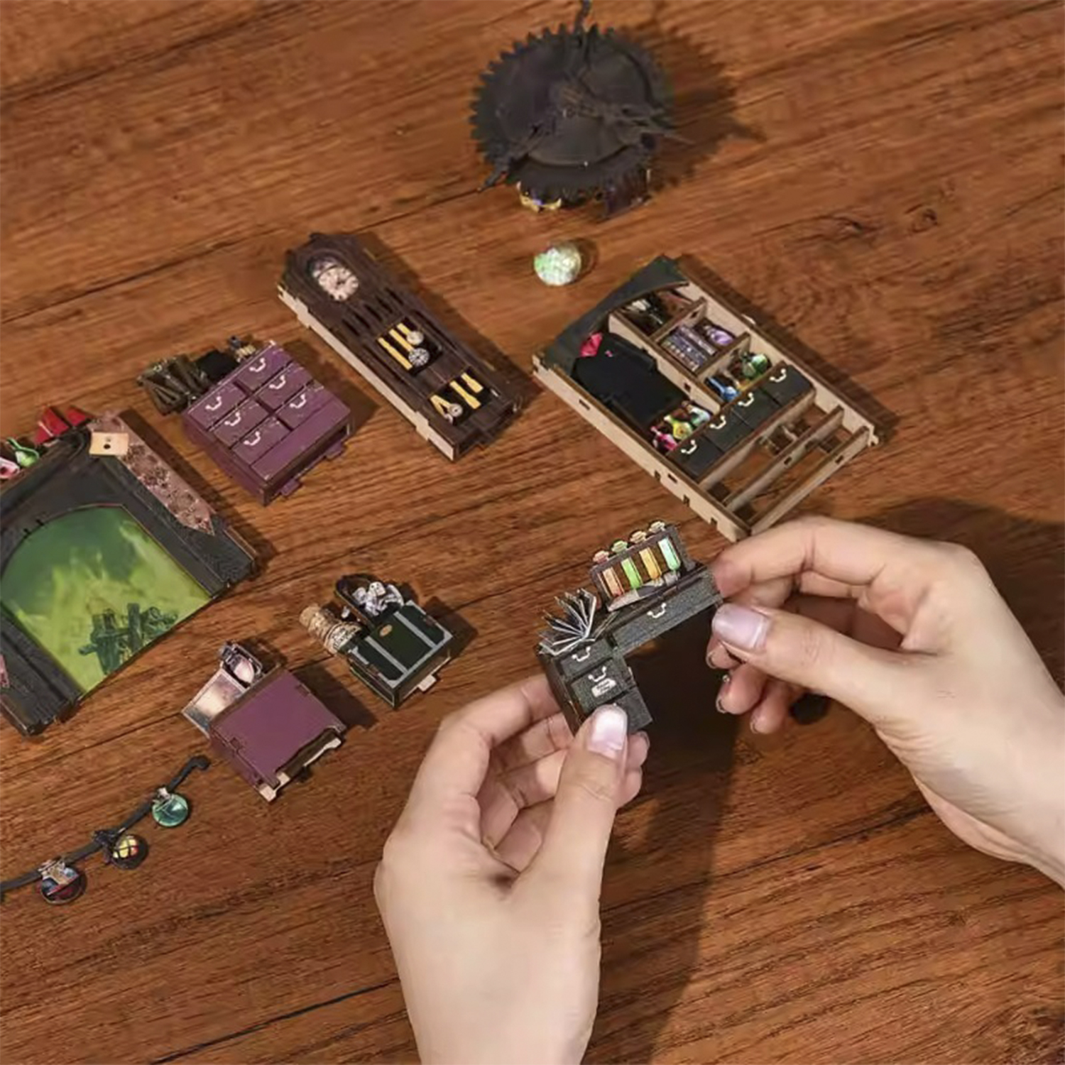 Mani che assemblano un mobile in miniatura con cassetti e libri su un tavolo di legno.