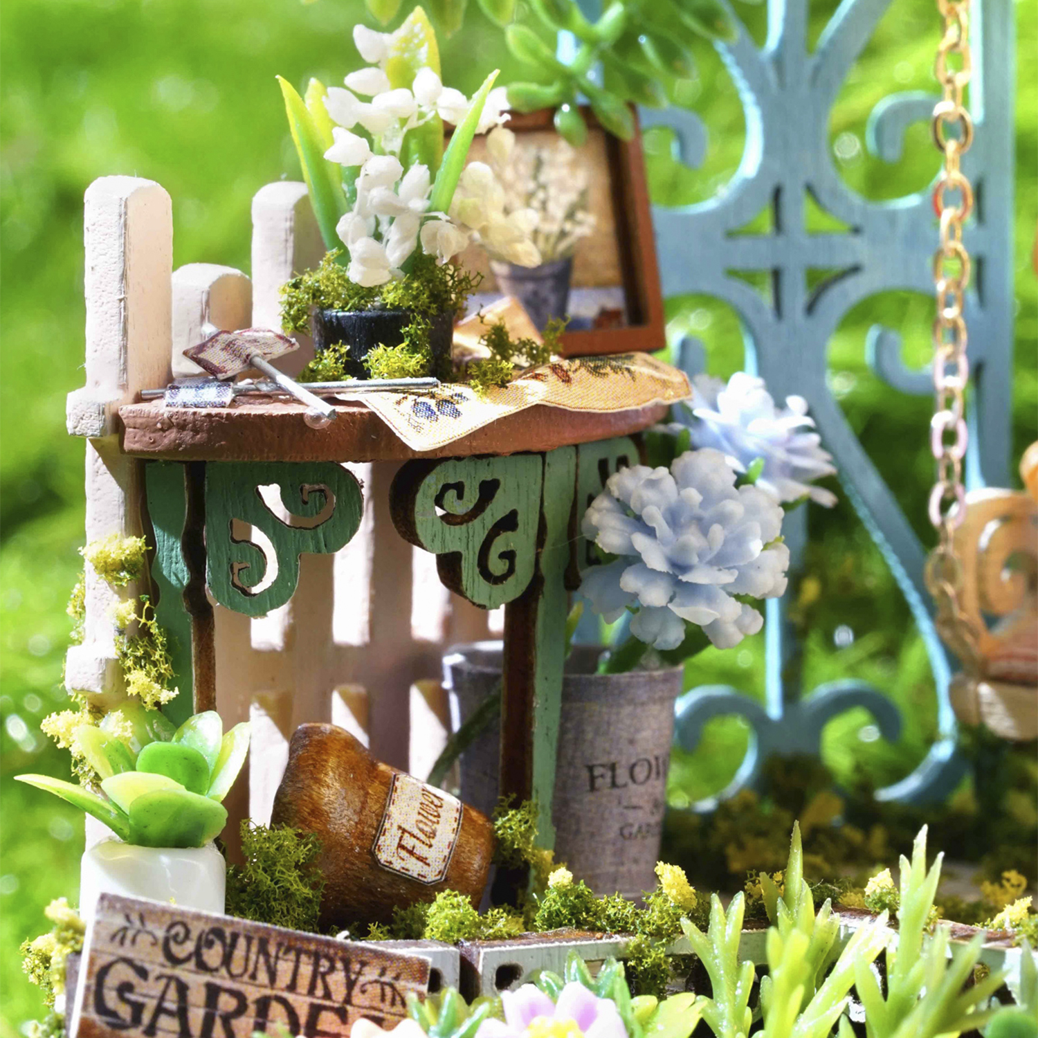 Scena di giardino in miniatura con piccoli fiori, una recinzione e un annaffiatoio.