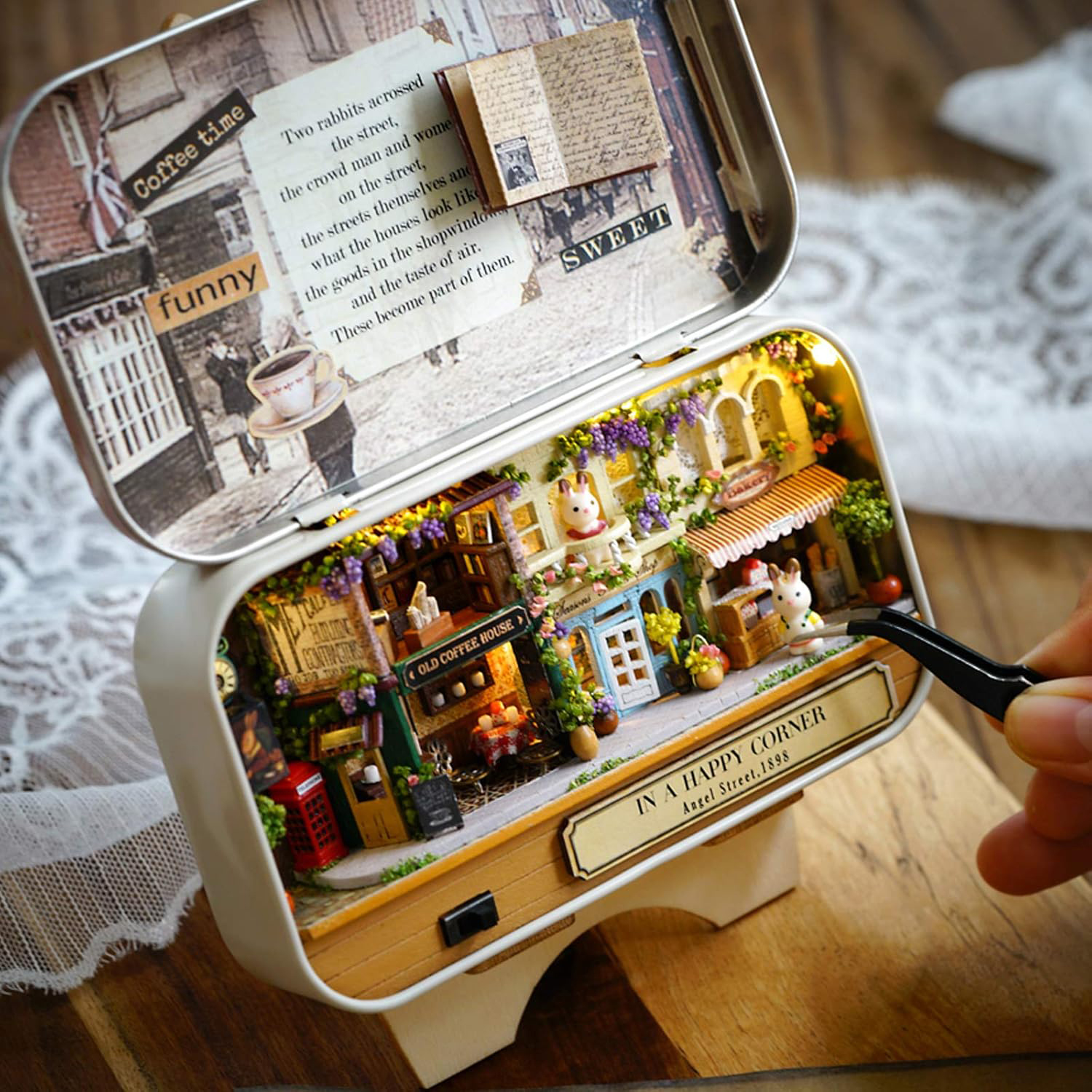 Scena in miniatura di una caffetteria con figure di conigli e luci, ispirata ai negozi vittoriani.