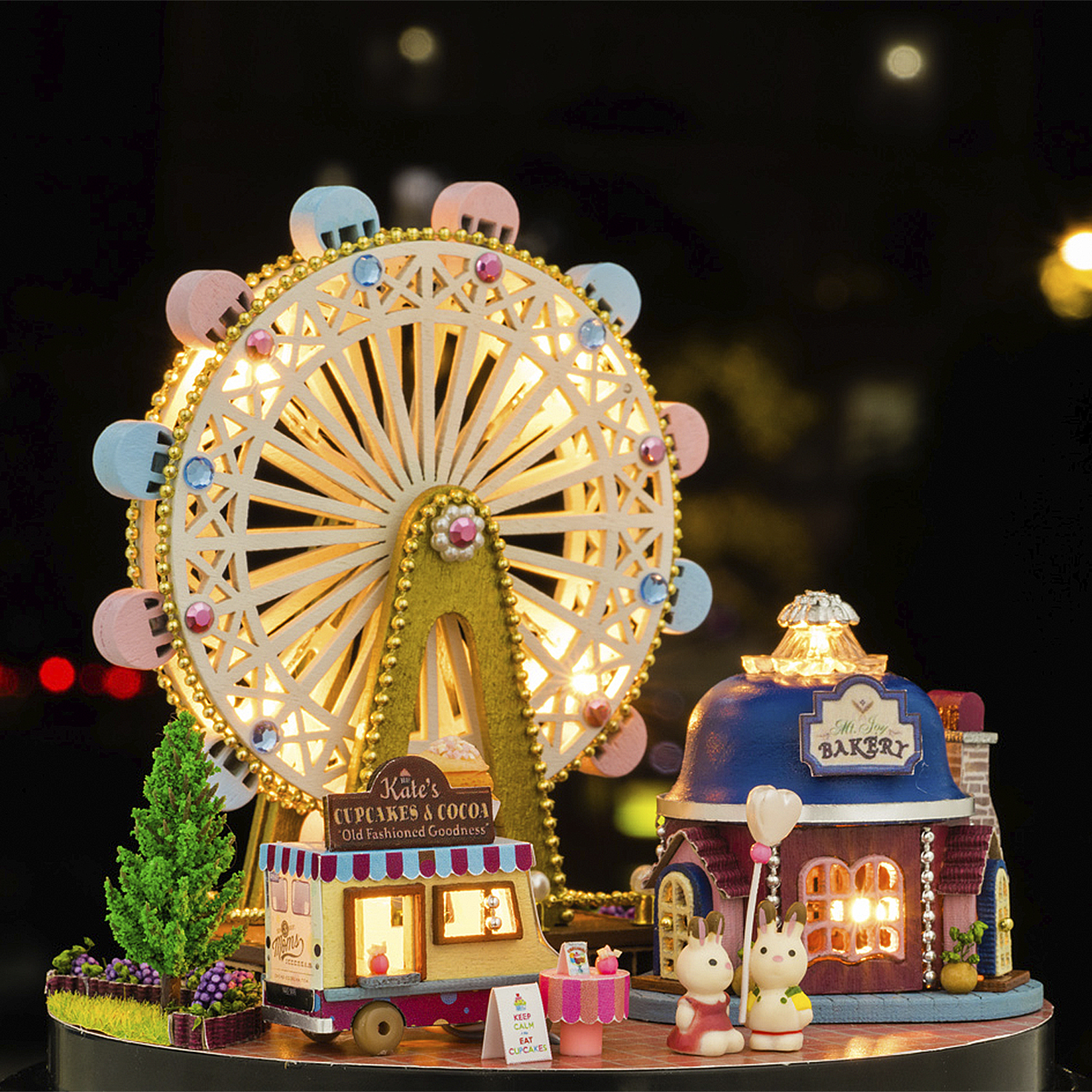 Parco divertimenti in miniatura con ruota panoramica illuminata, panificio, carretto cupcake e figure di conigli.