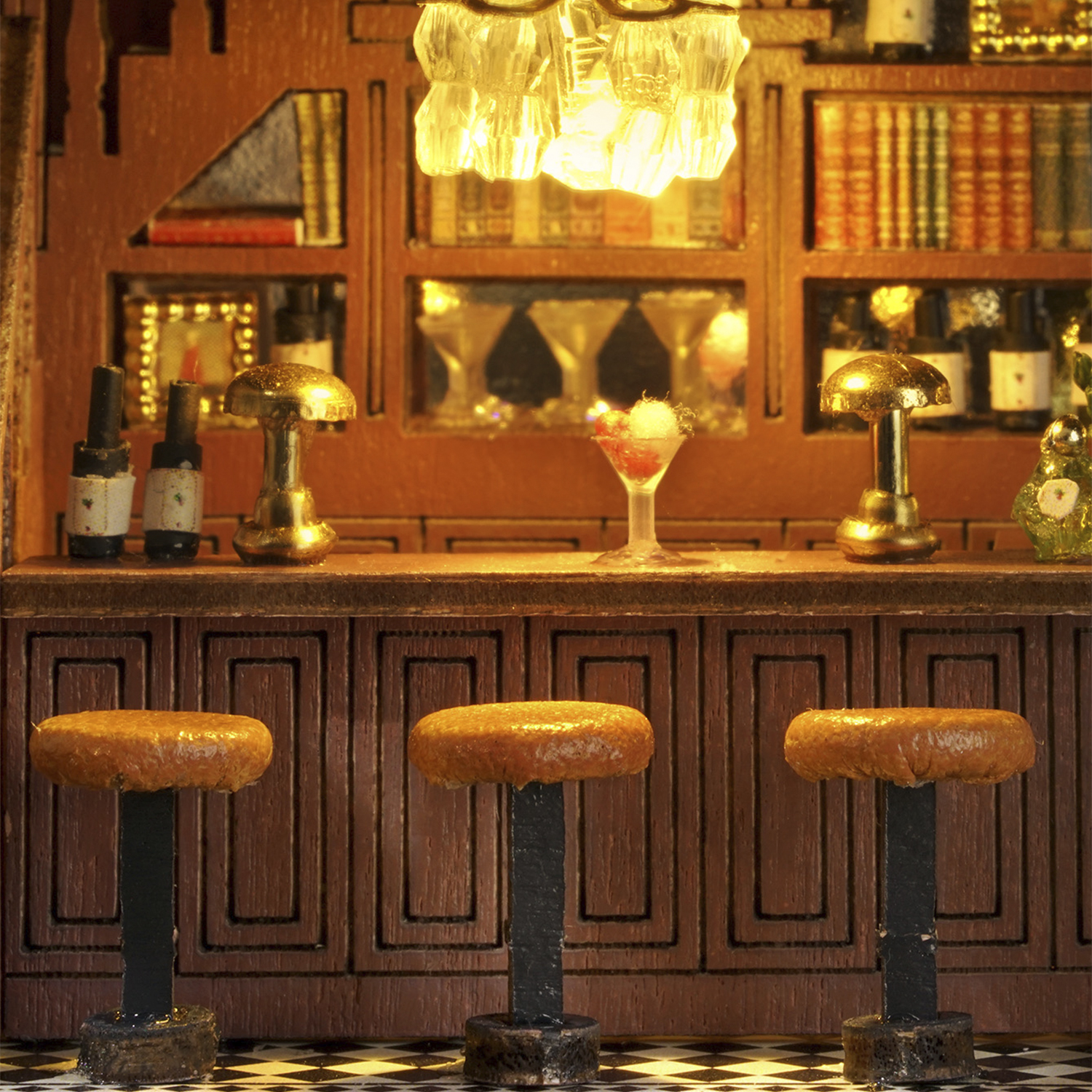 Una scena di bar in miniatura con tre sgabelli, bottiglie, bicchieri e libri.
