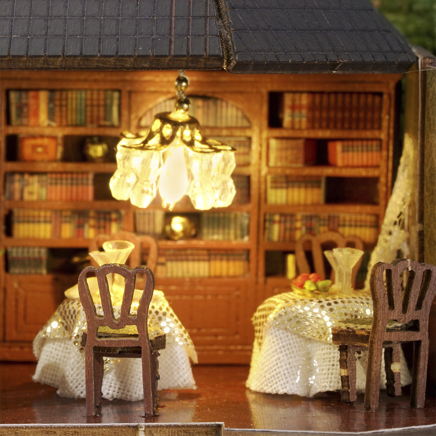 Biblioteca in miniatura con lampadario illuminato e tavoli apparecchiati.