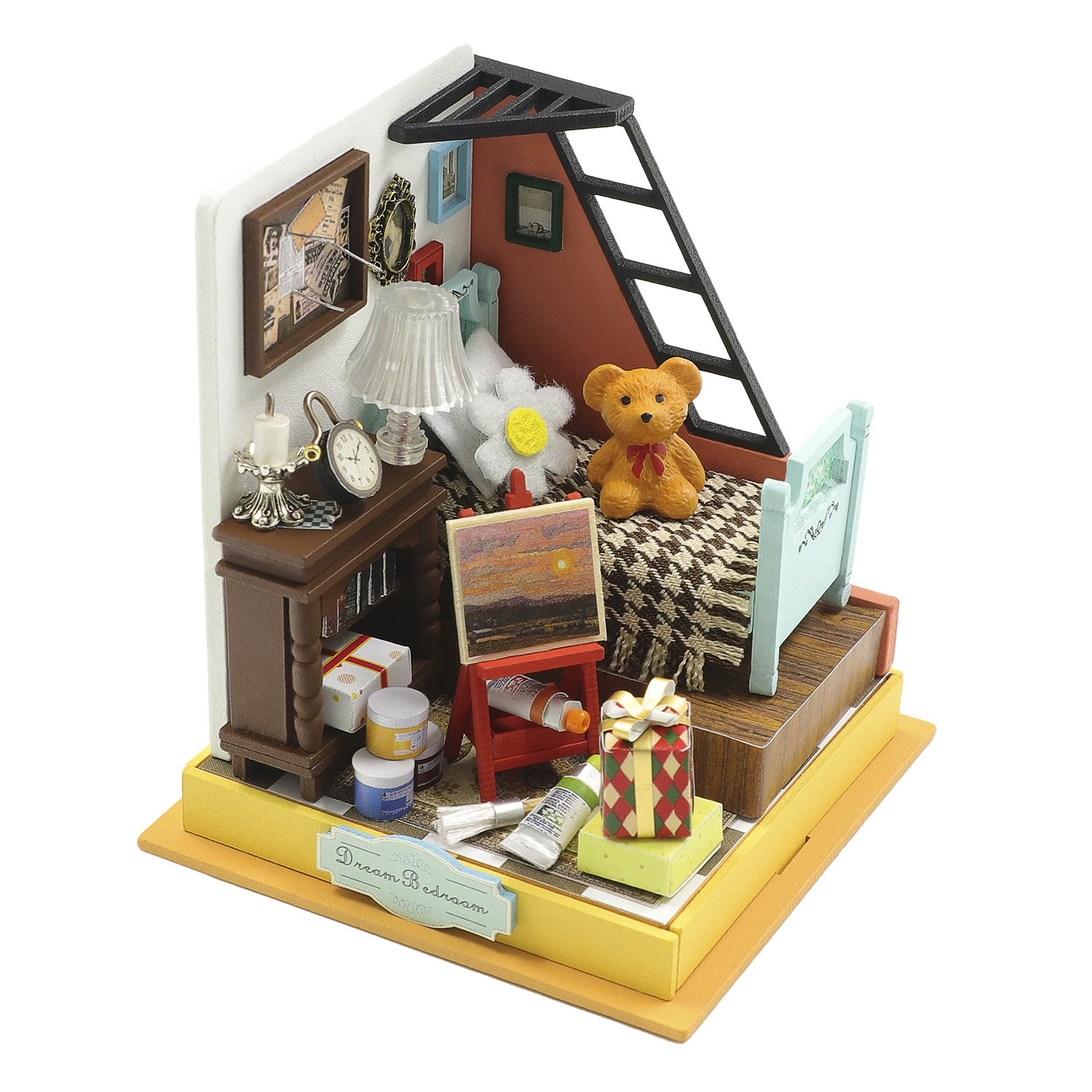 Stanza in miniatura con letto, orsacchiotto, cavalletto e libri. Decorata con quadri e lampada.
