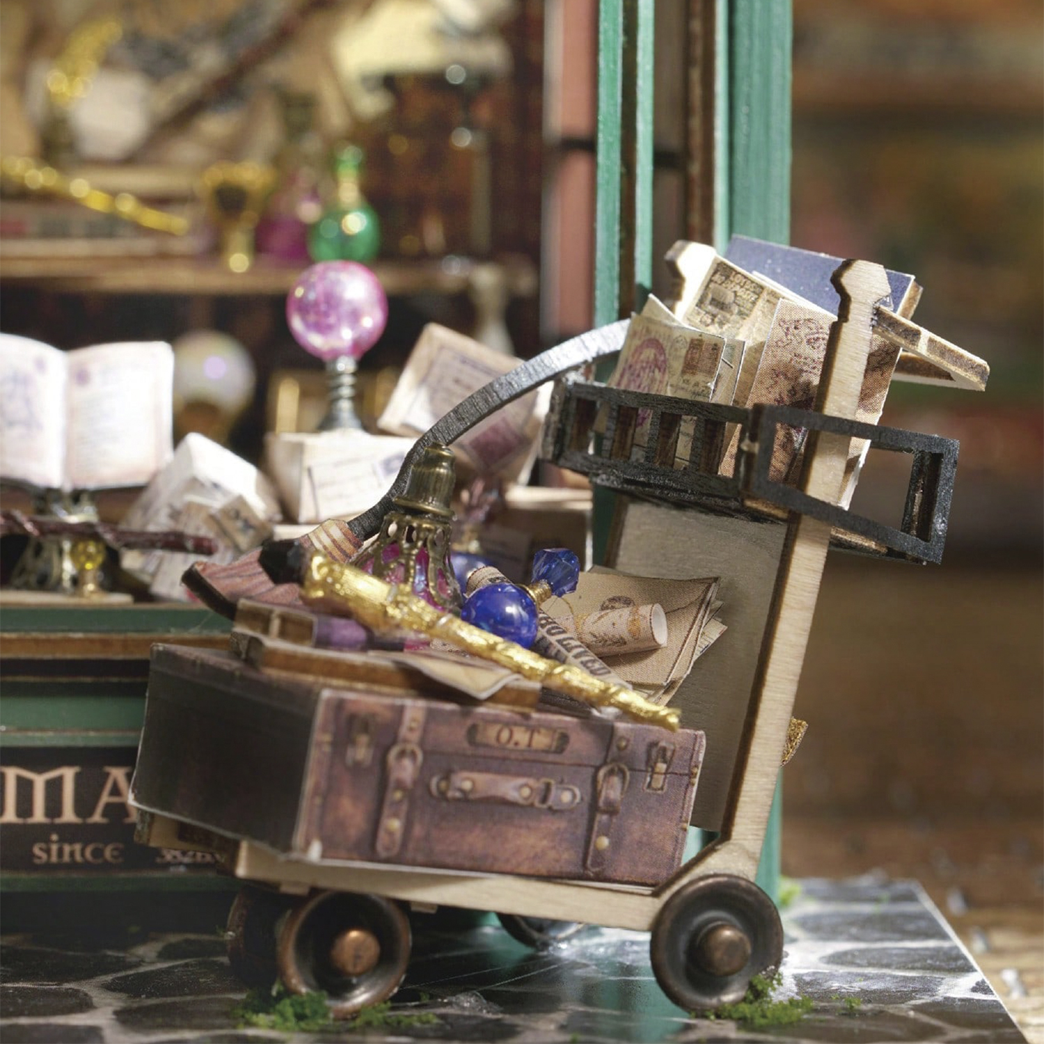 Un carrello in miniatura carico di valigia, libri e bottiglie.