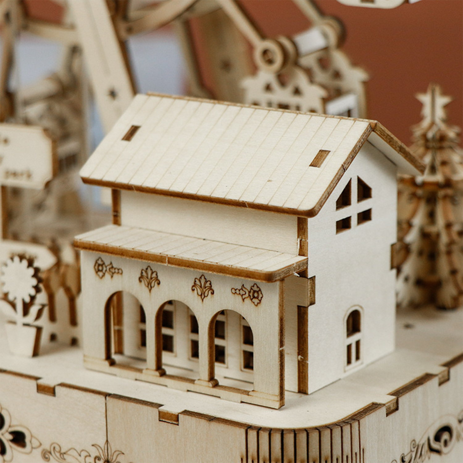 Una casa di legno in miniatura con portico è in primo piano. Sullo sfondo, un'attrazione del parco e un albero.