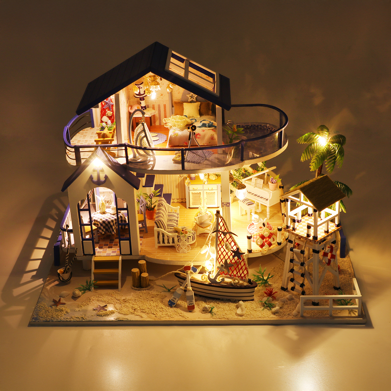 Casa sulla spiaggia in miniatura con luci, barca, torre di salvataggio.