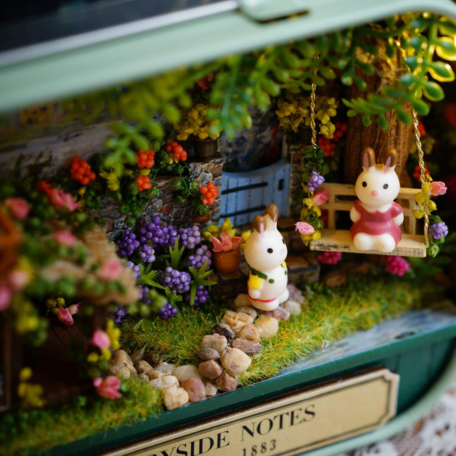 Due coniglietti in miniatura in un giardino con fiori, un'altalena e una piccola porta.