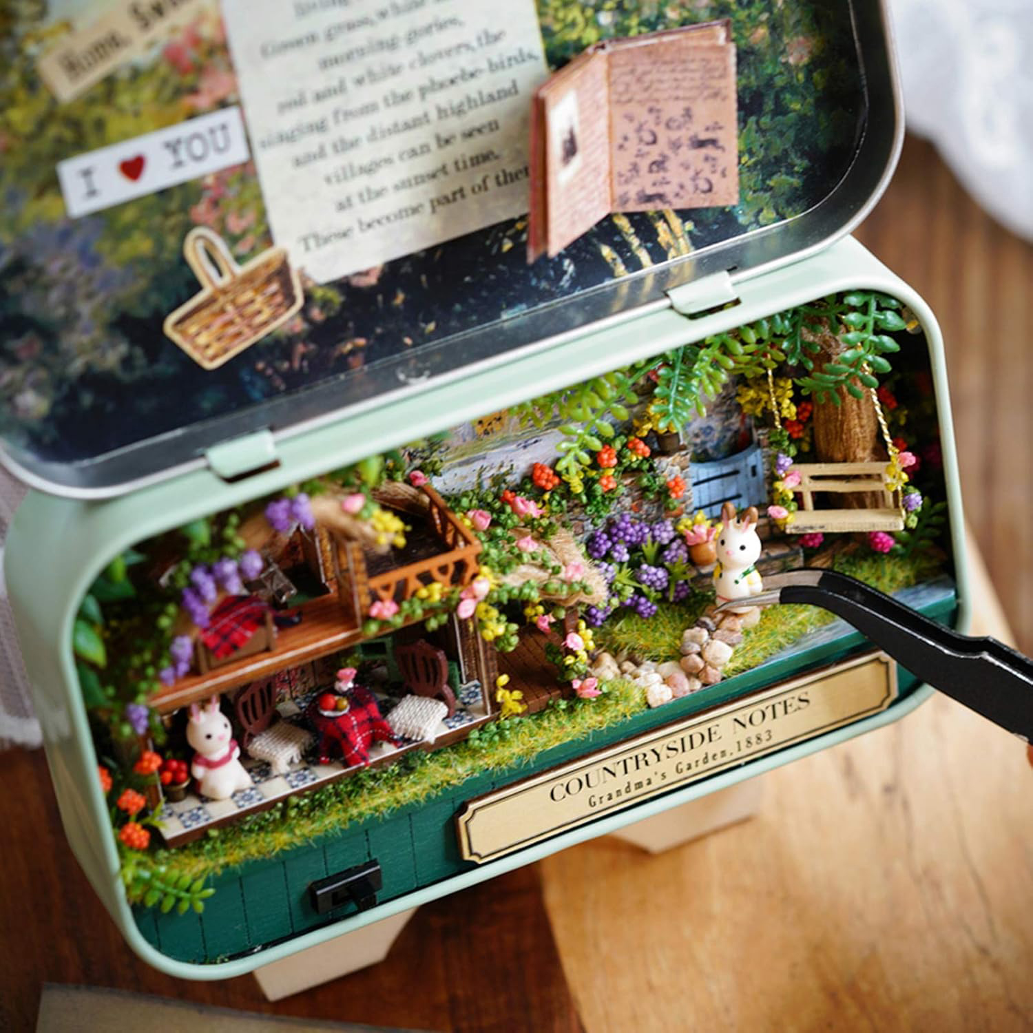 Scena di giardino in miniatura in una scatola con case, conigli e fiori.