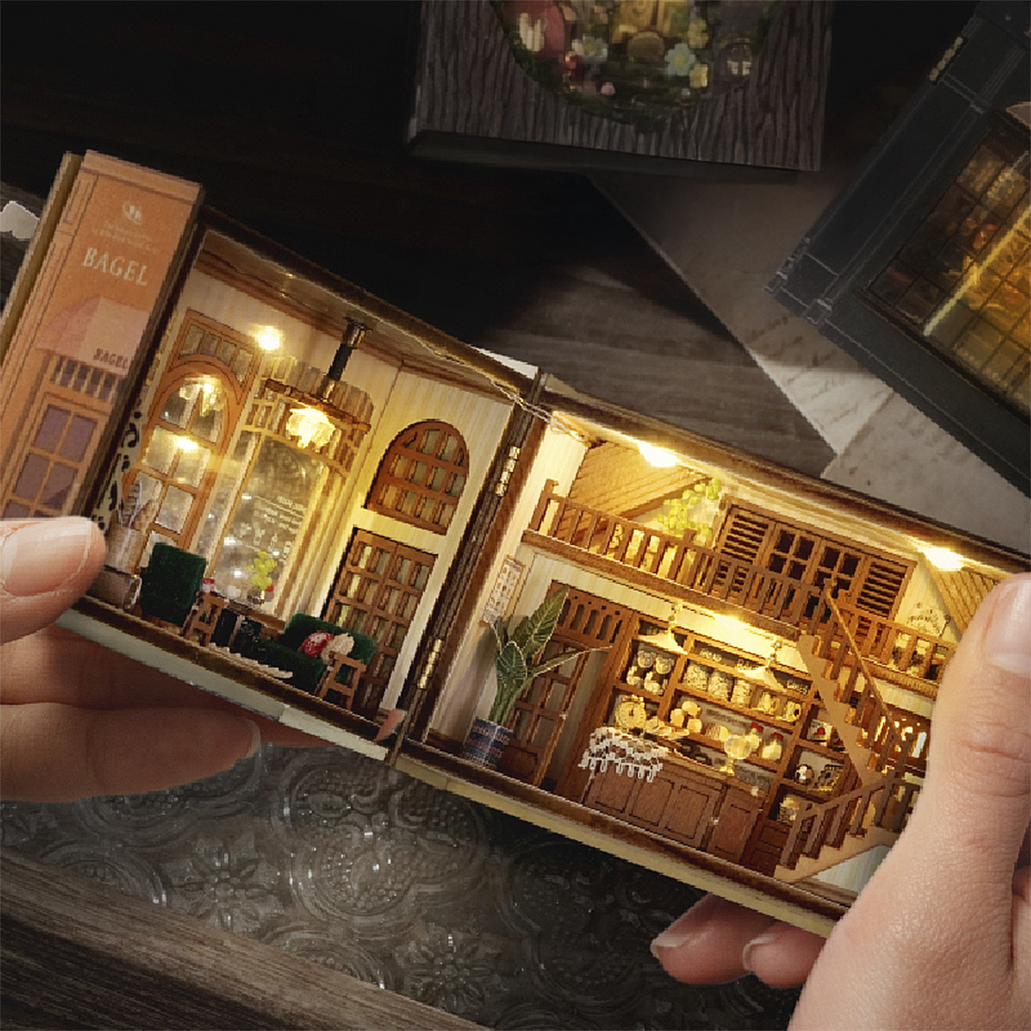 Casa libro in miniatura con mobili, scaffali e luci, tenuta dalle mani.