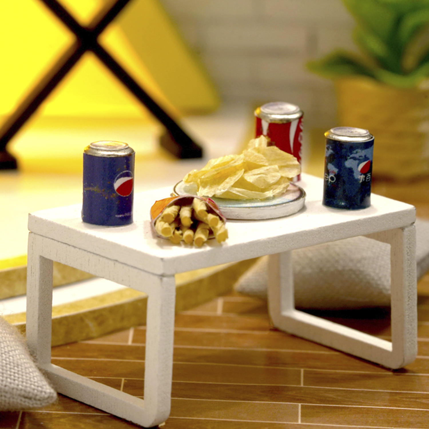 Tavolino in miniatura con lattine di soda, patatine e cracker.