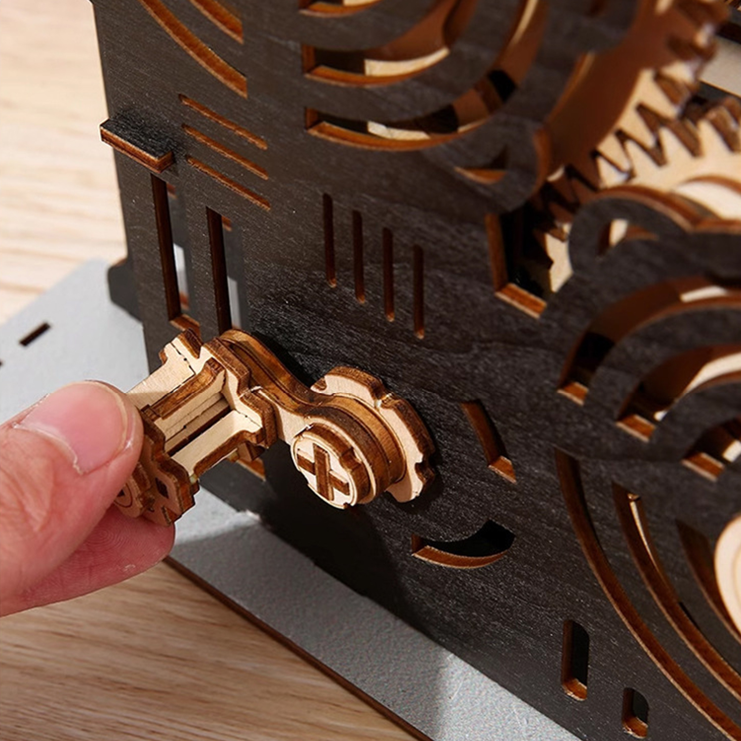 Un dito gira una leva di legno su una struttura in legno scuro con ingranaggi.