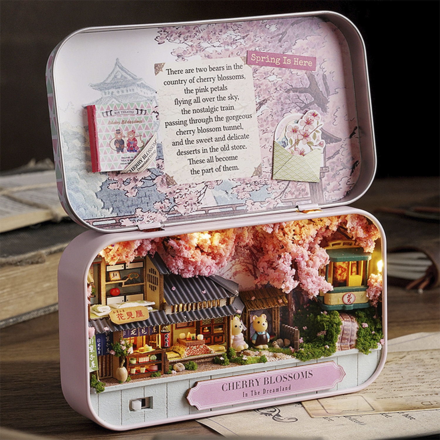 Un diorama in una scatola rosa con fiori di ciliegio, una casa, due orsi e un piccolo treno.