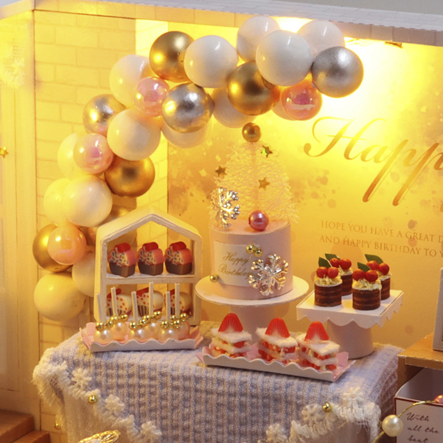 Scena di compleanno in miniatura con torta, cupcake, mele caramellate e arco di palloncini.