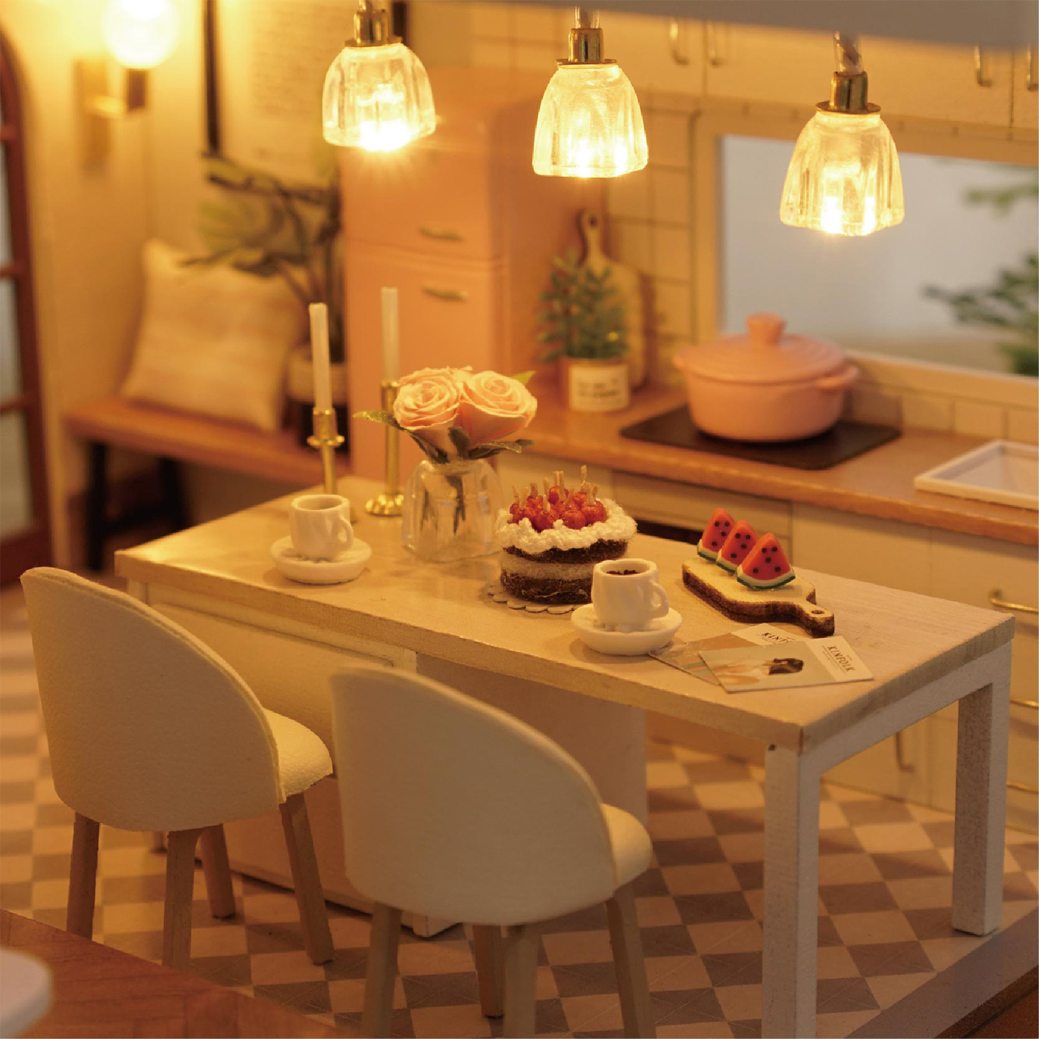 Cucina in miniatura con tavolo, due sedie, torta, frutta e frigorifero rosa.