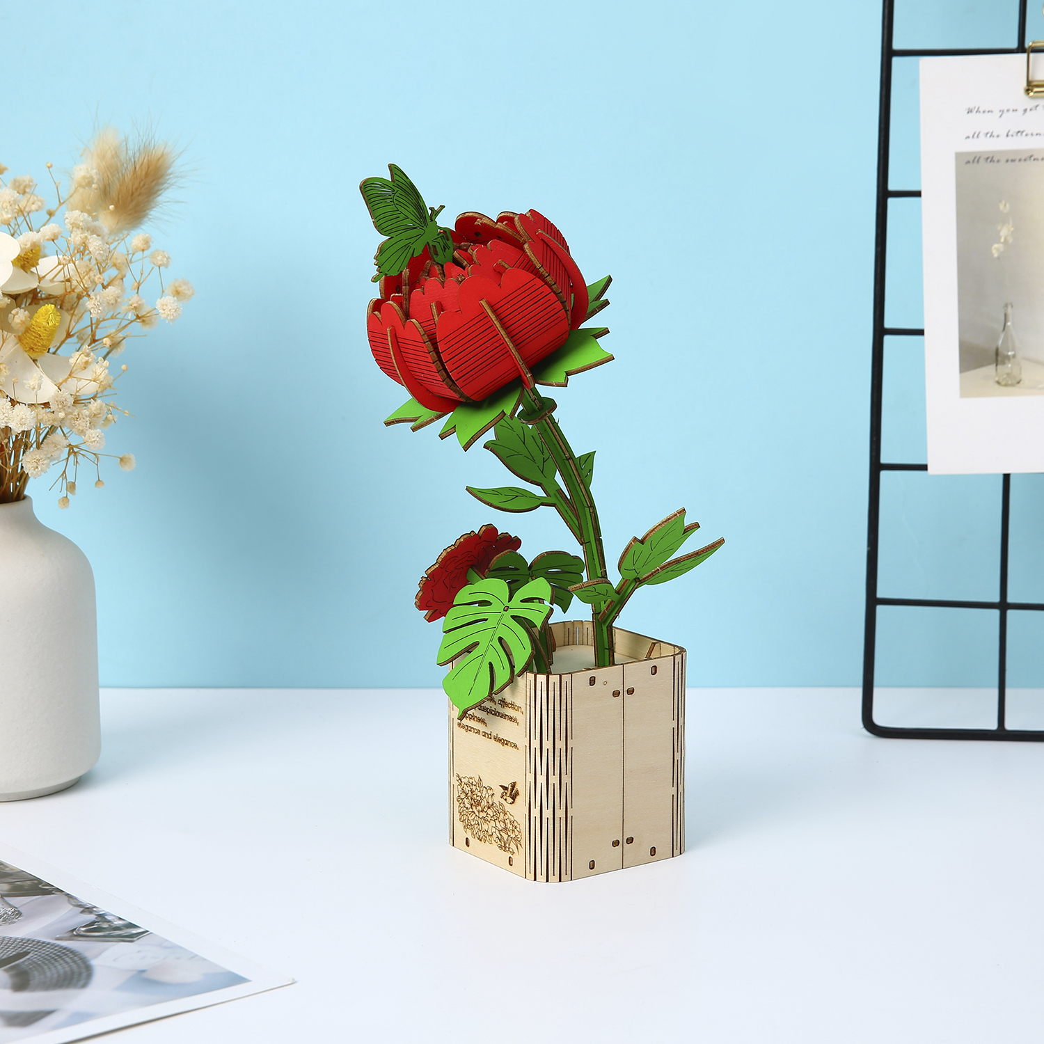 Un modello di rosa rossa in legno con una farfalla in un vaso di legno su sfondo blu.
