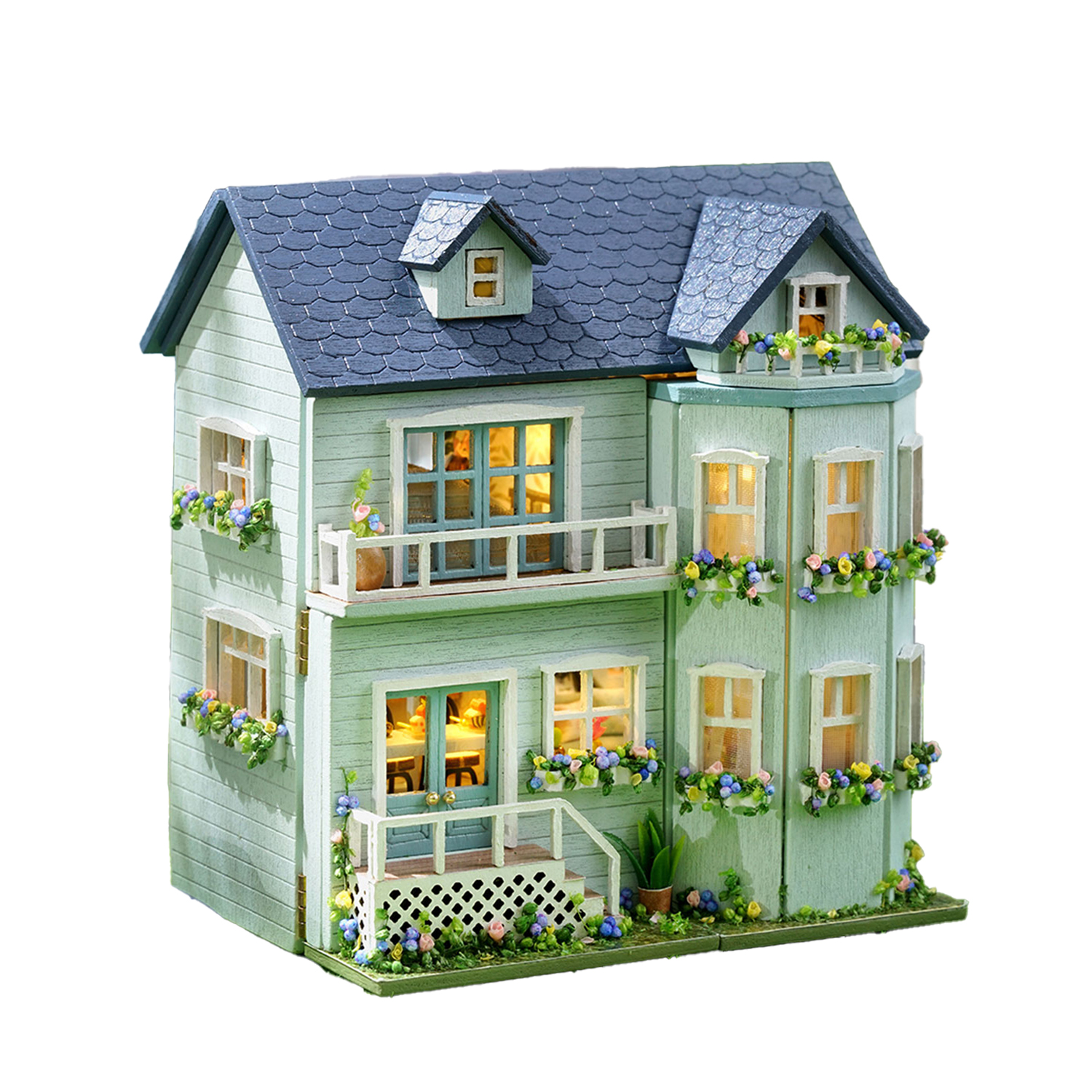 Una casa delle bambole verde chiaro con tegole blu, fioriere e finestre illuminate.