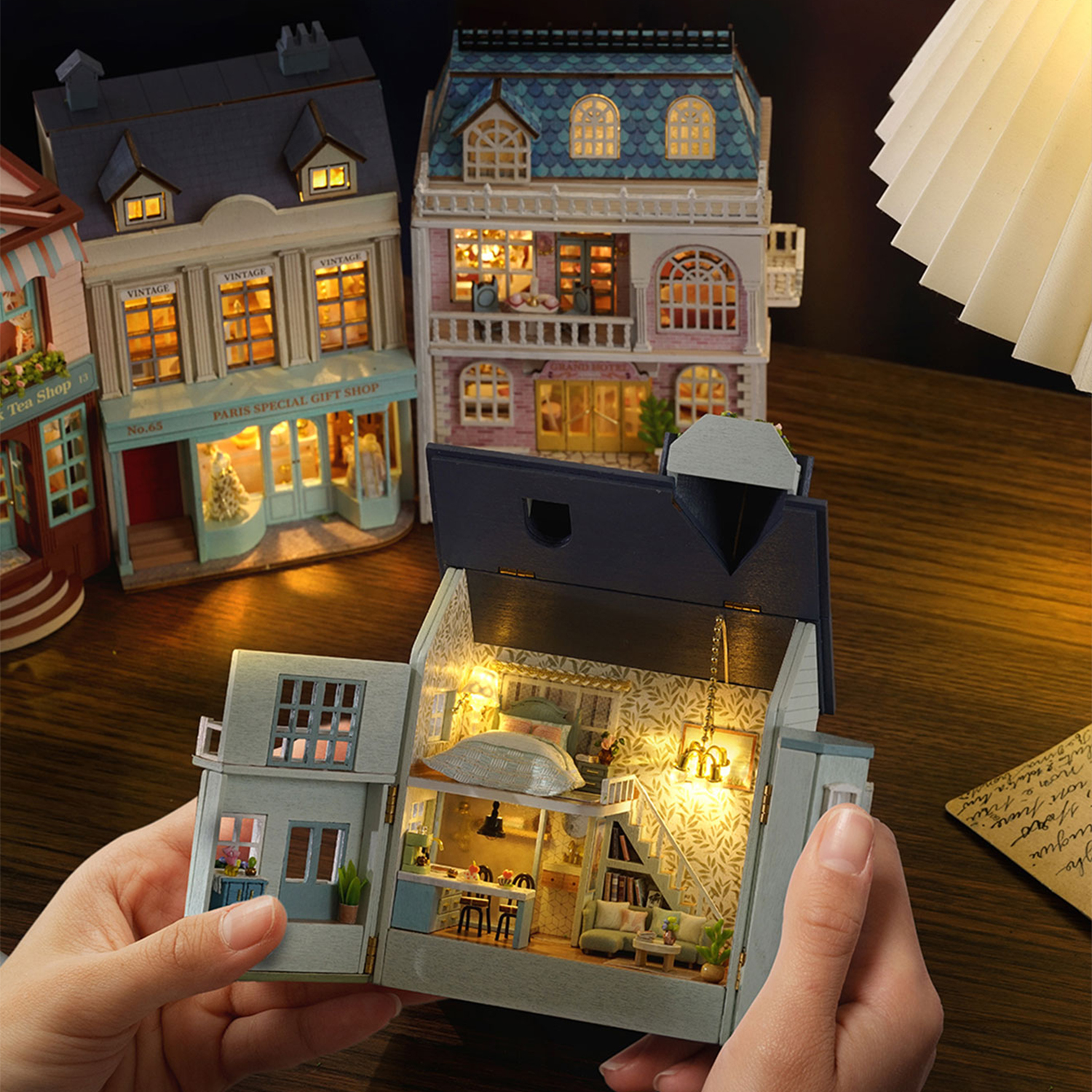Case in miniatura illuminate su tavolo di legno, una tenuta dalle mani.
