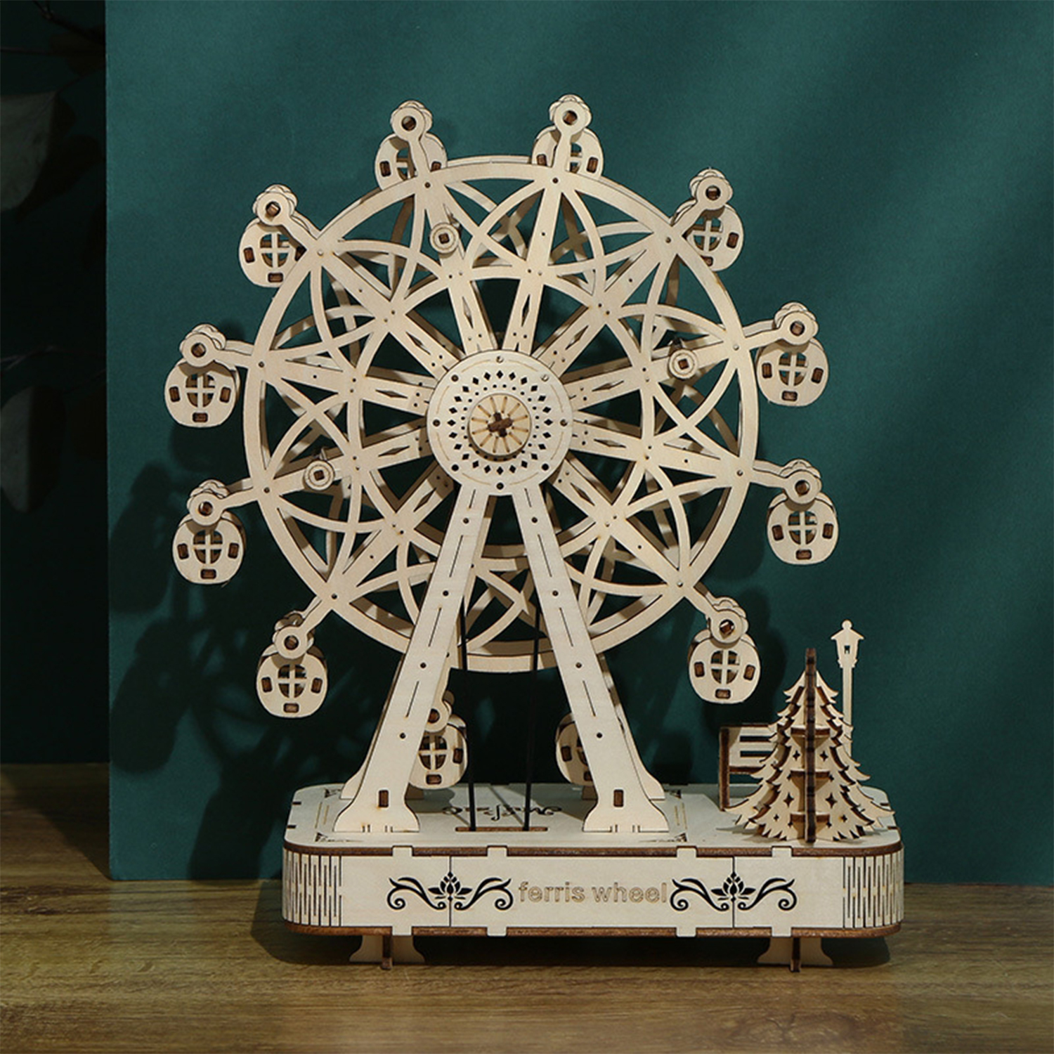 Un modello di ruota panoramica in legno con gondole, un albero e un lampione.