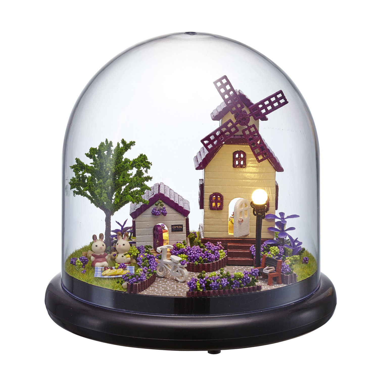 Villaggio in miniatura con mulino, conigli e fiori sotto una cupola di vetro.