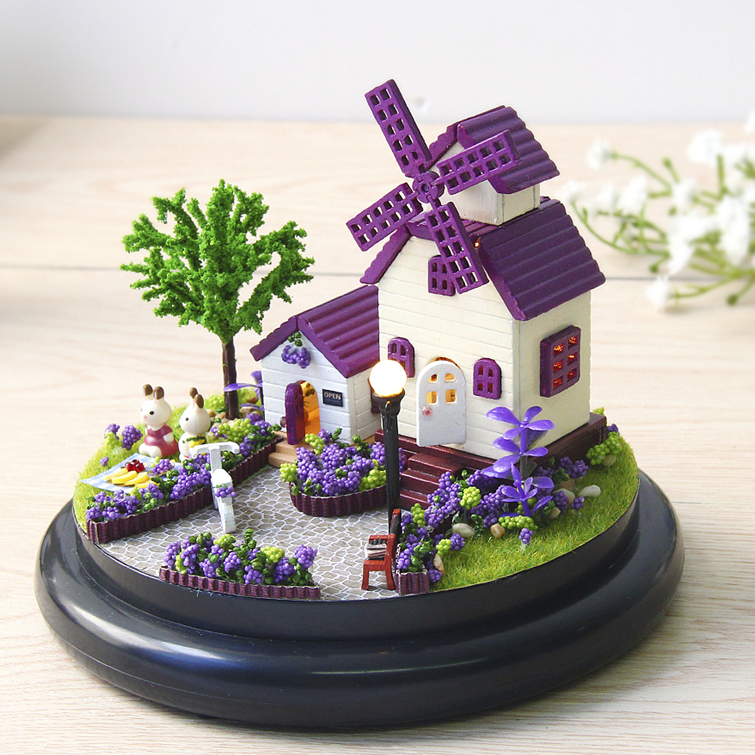 Casa mulino in miniatura con alberi, fiori e figure di conigli su base nera.
