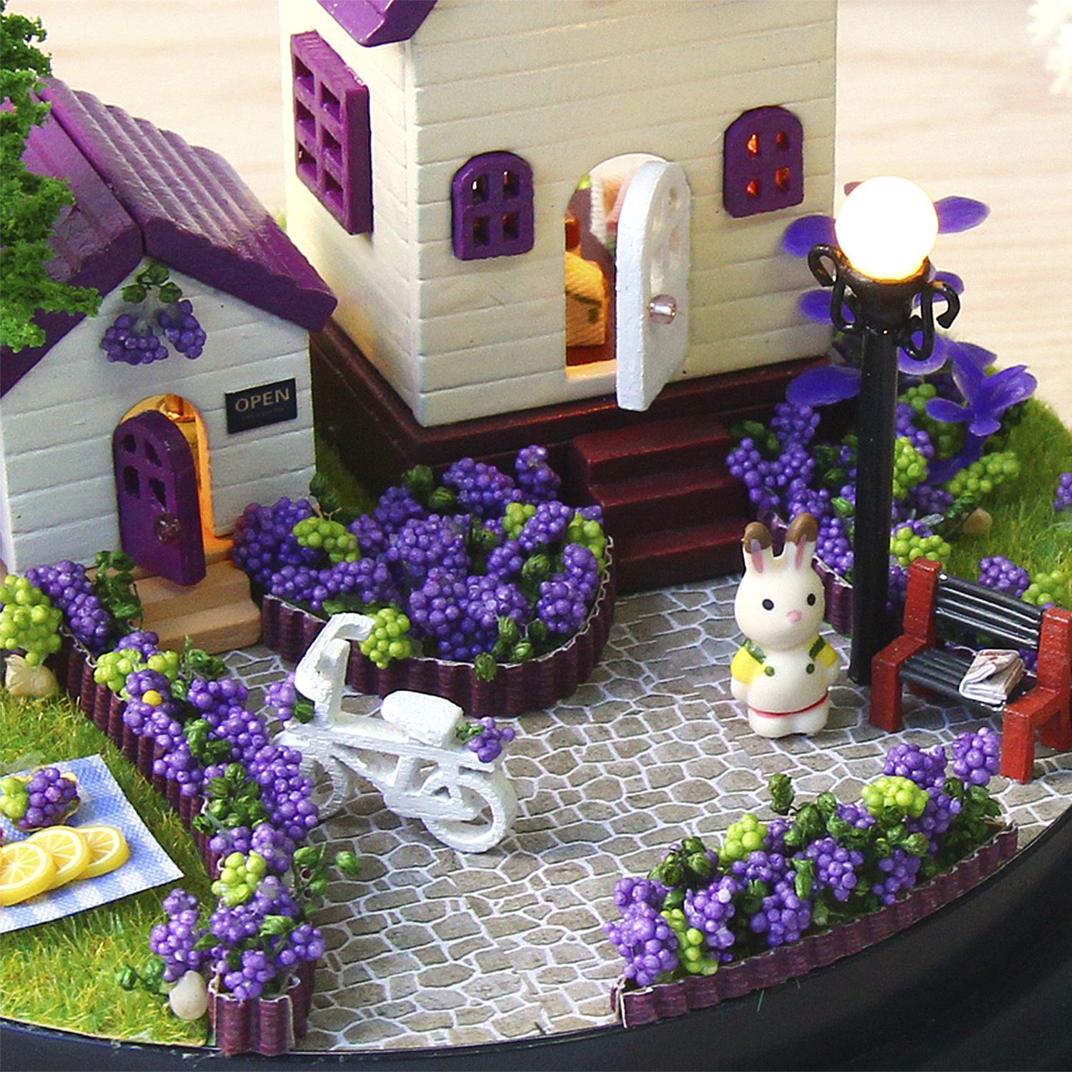 Casa in miniatura con uva viola, bicicletta, coniglietto e panchina.