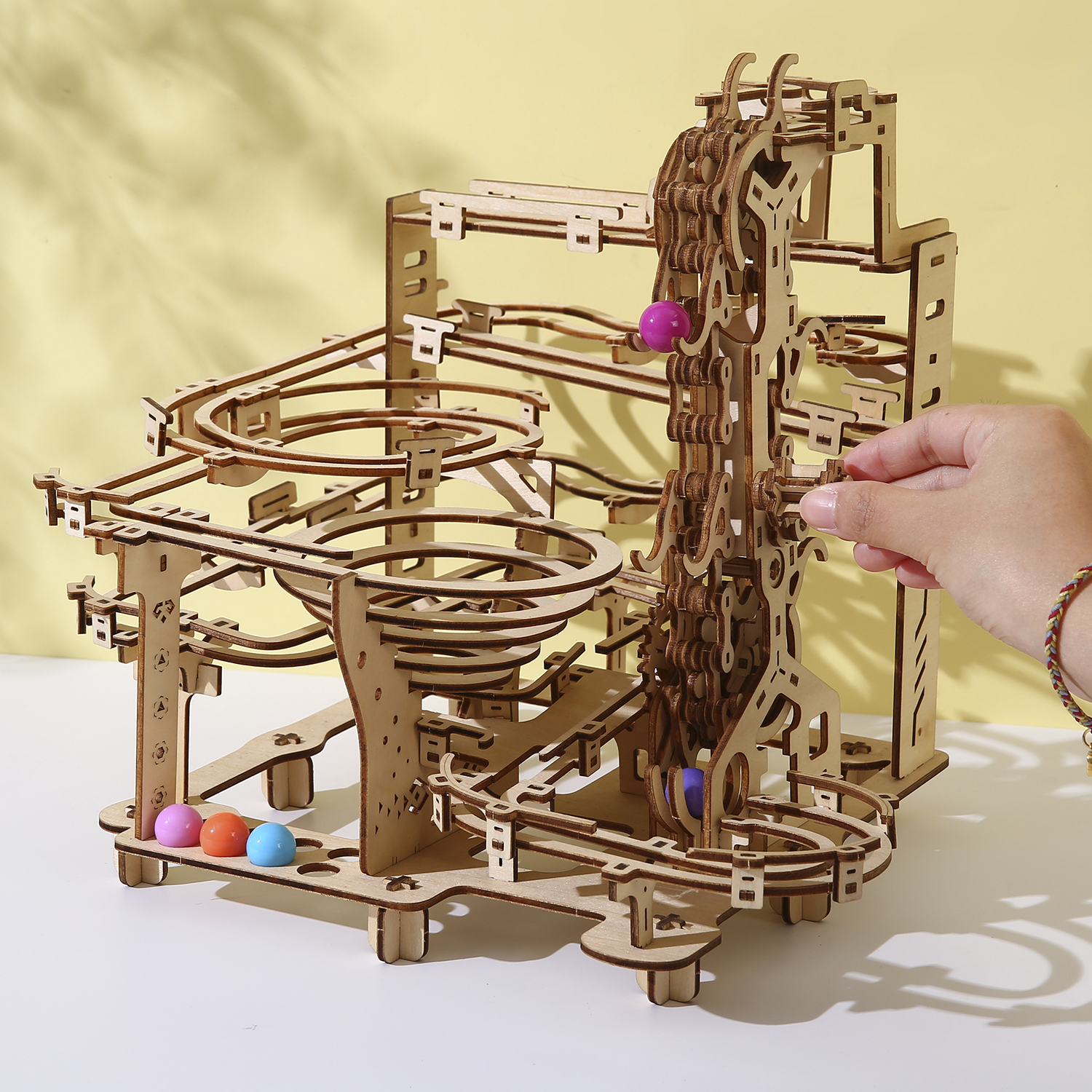 Un modello di pista per biglie in legno con palline colorate e una mano.