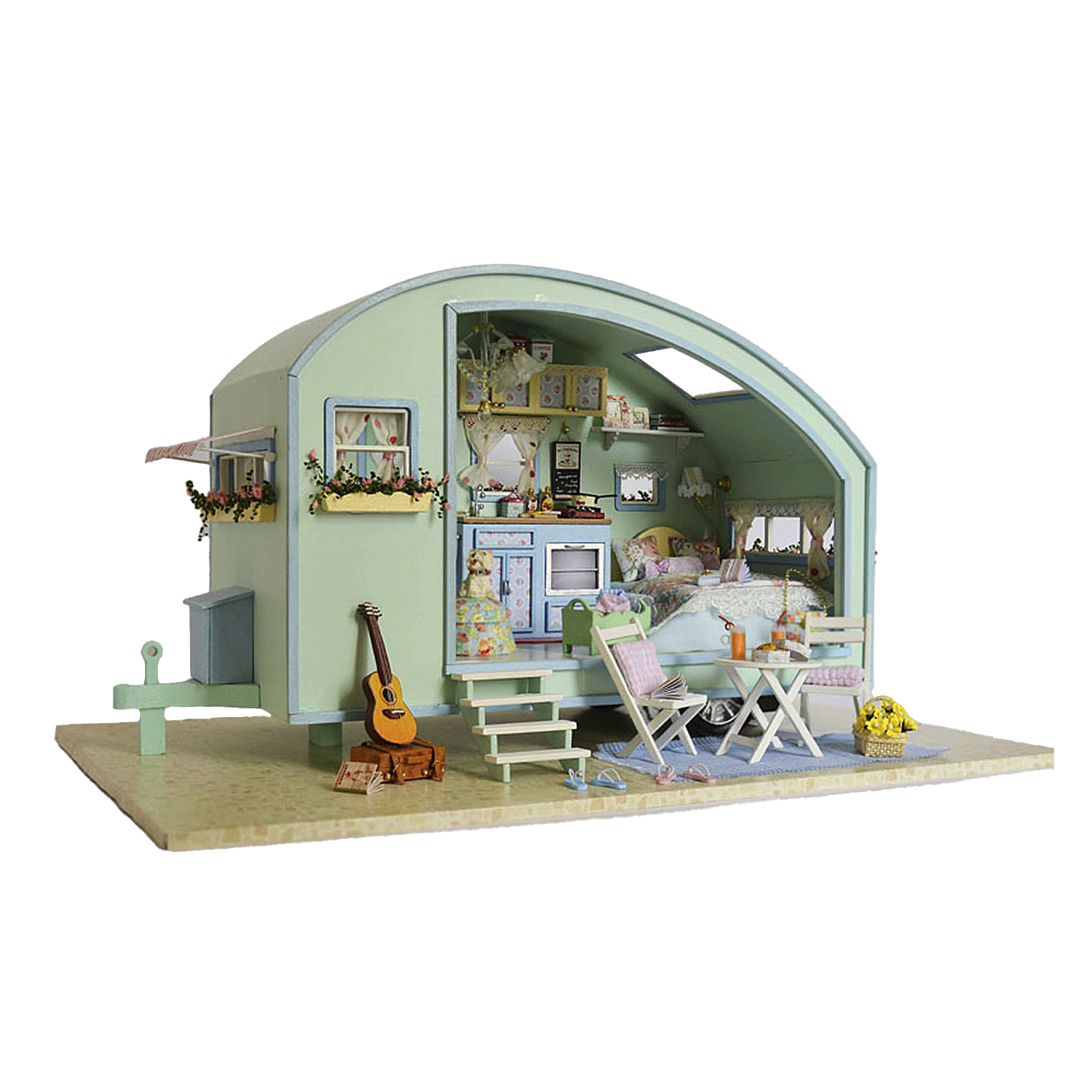 Camper in miniatura con letto, tavolo, sedie, chitarra e fiori.