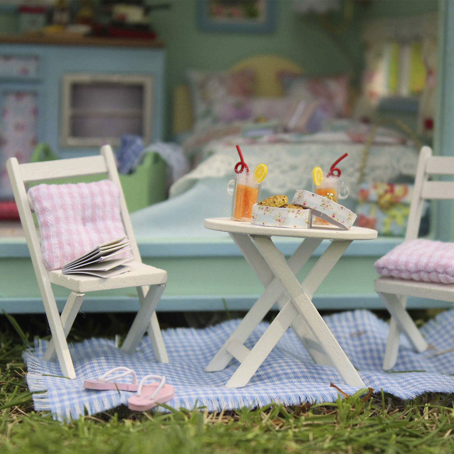 Scena di picnic in miniatura all'aperto con due sedie, tavolo, bevande e biscotti.