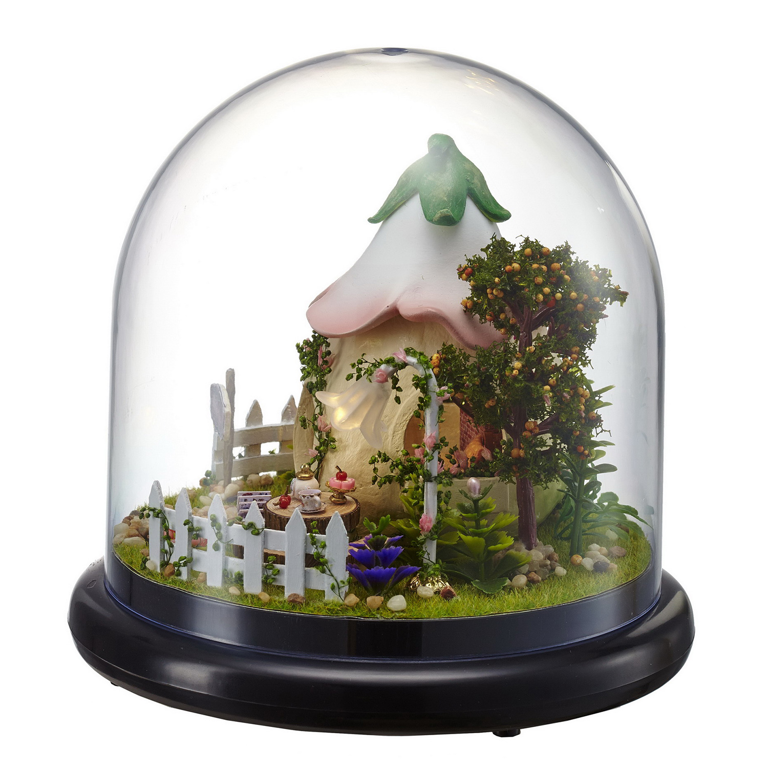 Mini casa delle fate sotto campana di vetro con recinzione, albero e fiori.