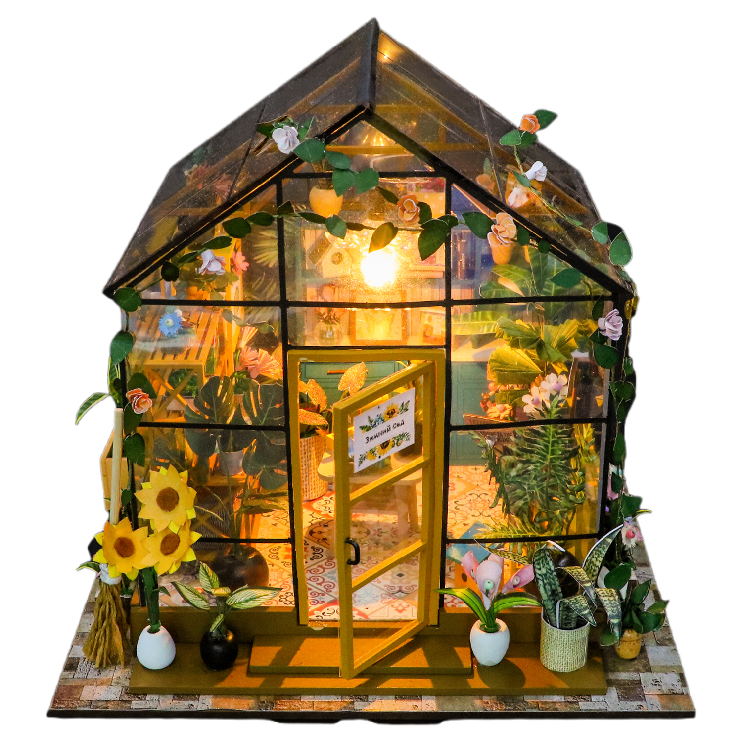 Una serra in miniatura con piante e fiori, illuminata dall'interno. Girasoli all'esterno.