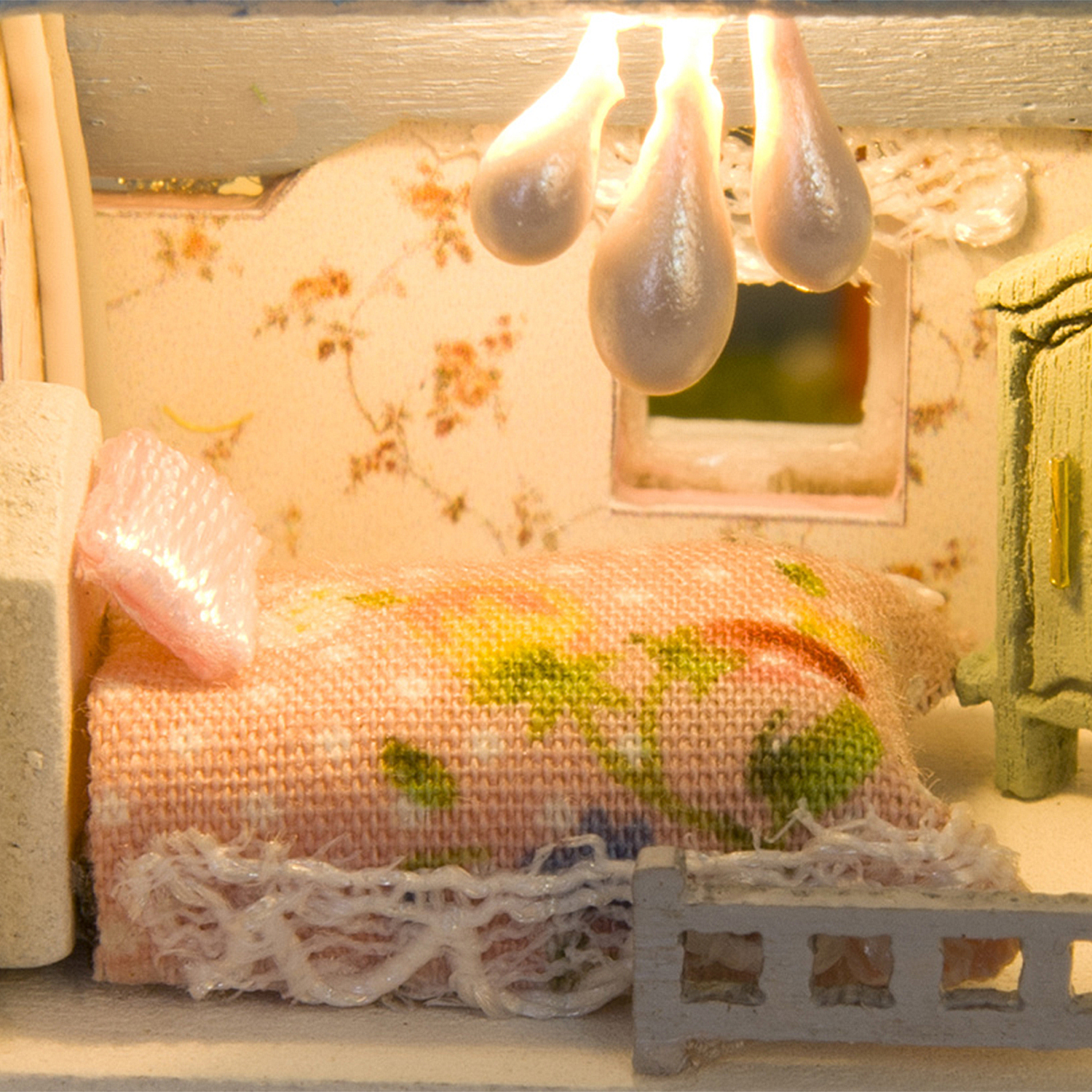 Letto in miniatura con motivo floreale, coperta rosa e una lampada.